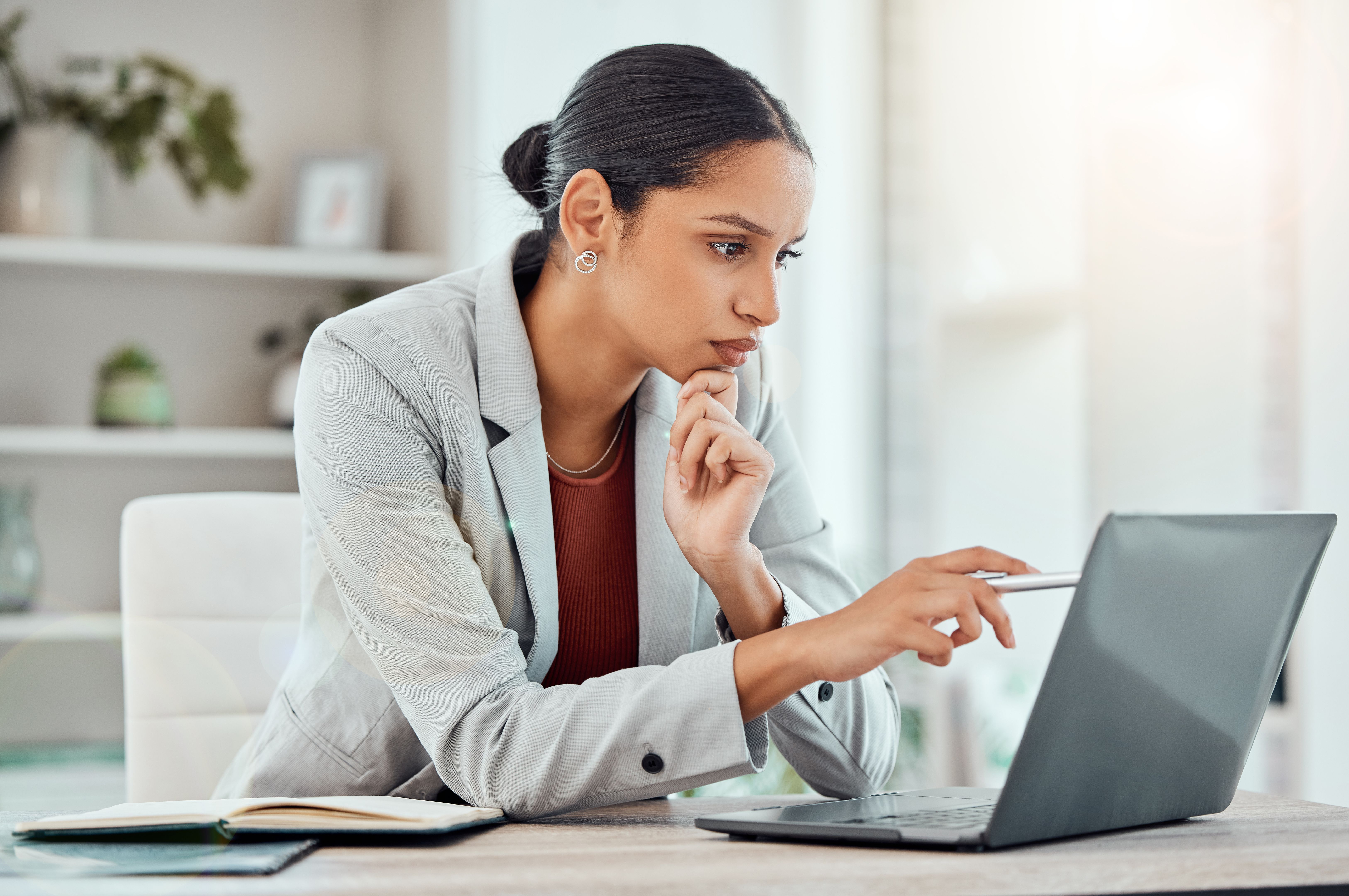 Serious, laptop and professional businesswoman sitting and reading a work email with a pen working from home. Business, computer and focused female lawyer in modern office preparing for a case. Serious, laptop and professional businesswoman sitting and reading a work email with a pen working from home. Business, computer and focused female lawyer in modern office preparing for a case.