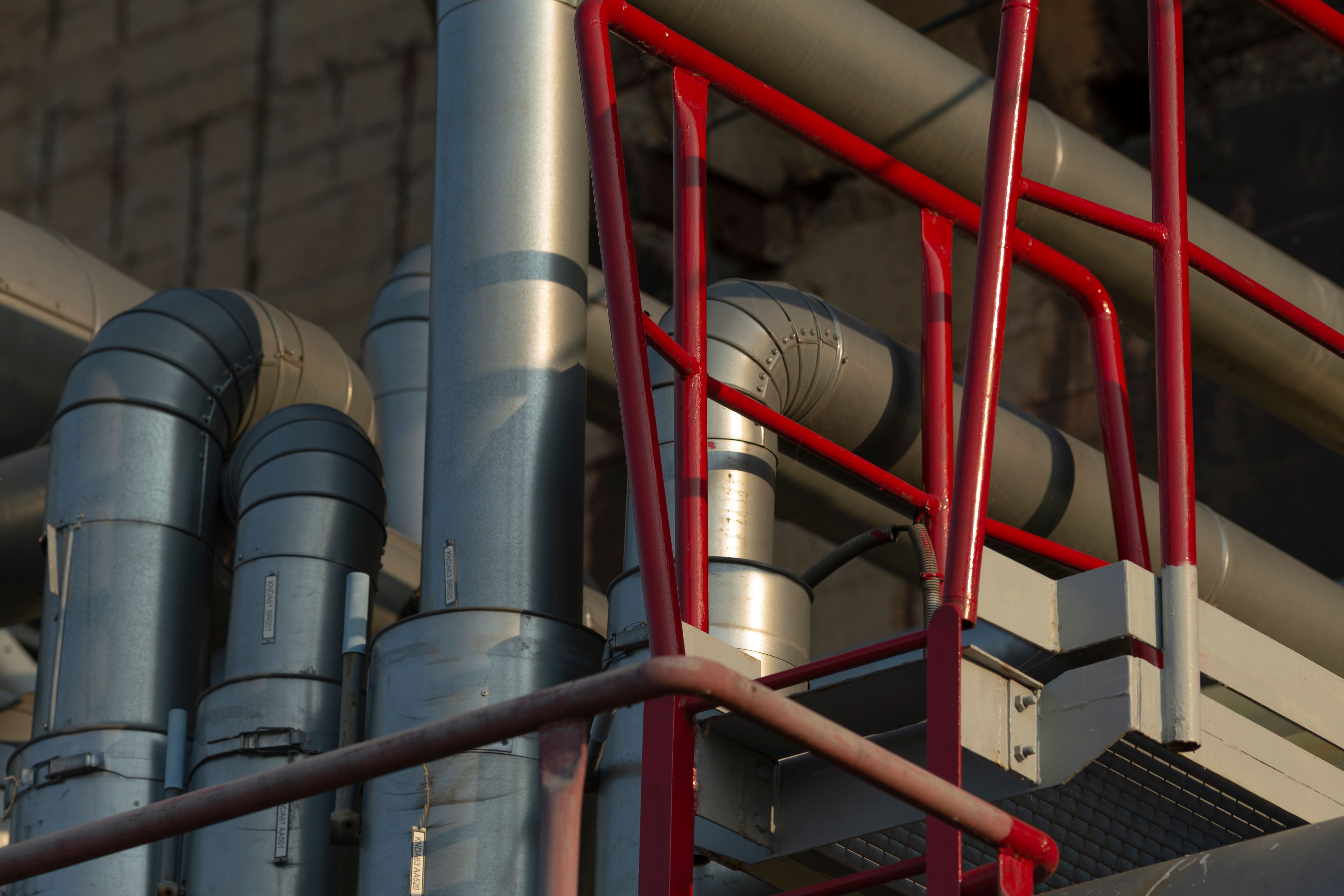 A collection of pipes is interconnected with a striking red railing A collection of pipes is interconnected with a striking red railing
