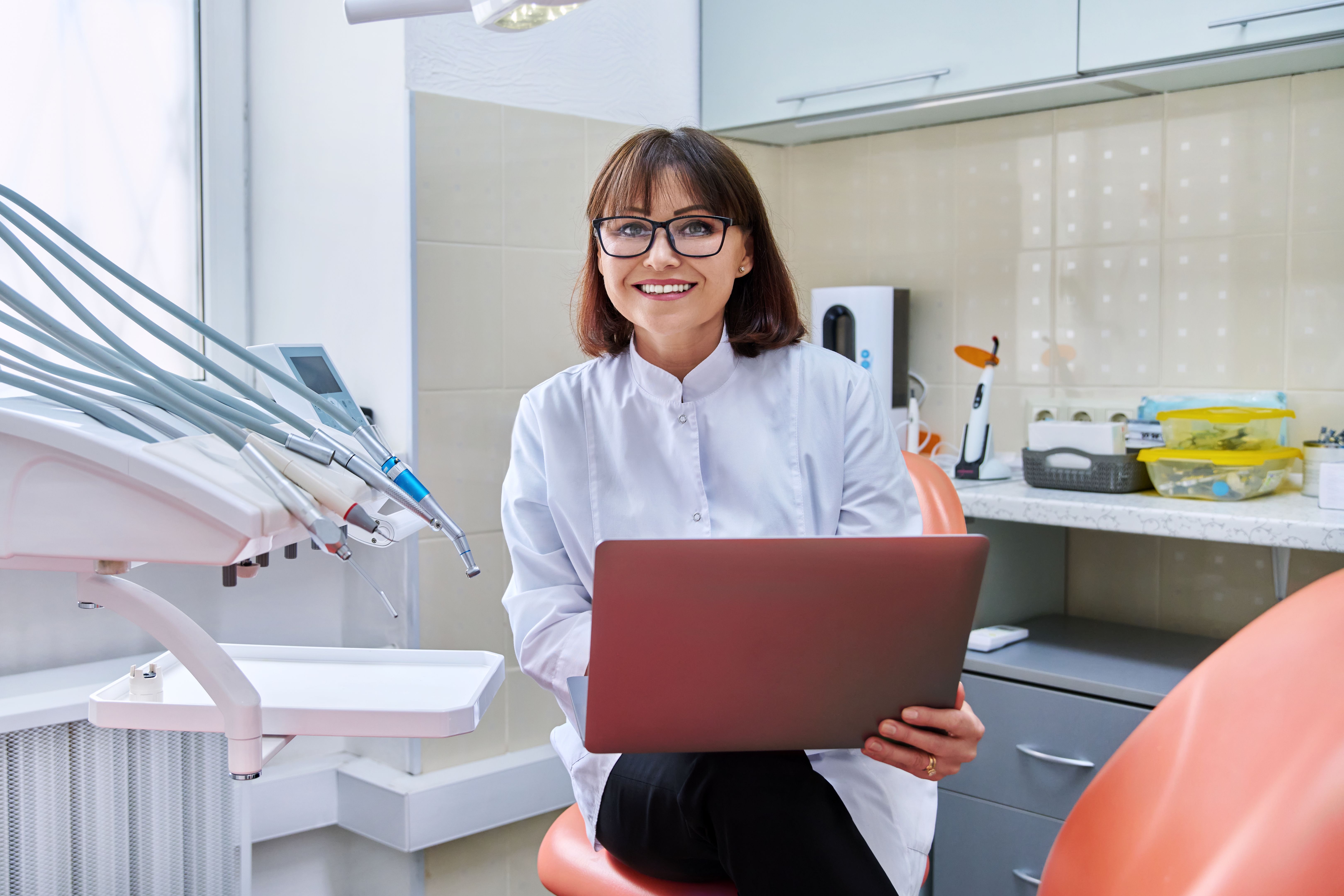 Portrait of doctor sitting in office with laptop in her hands looking at camera