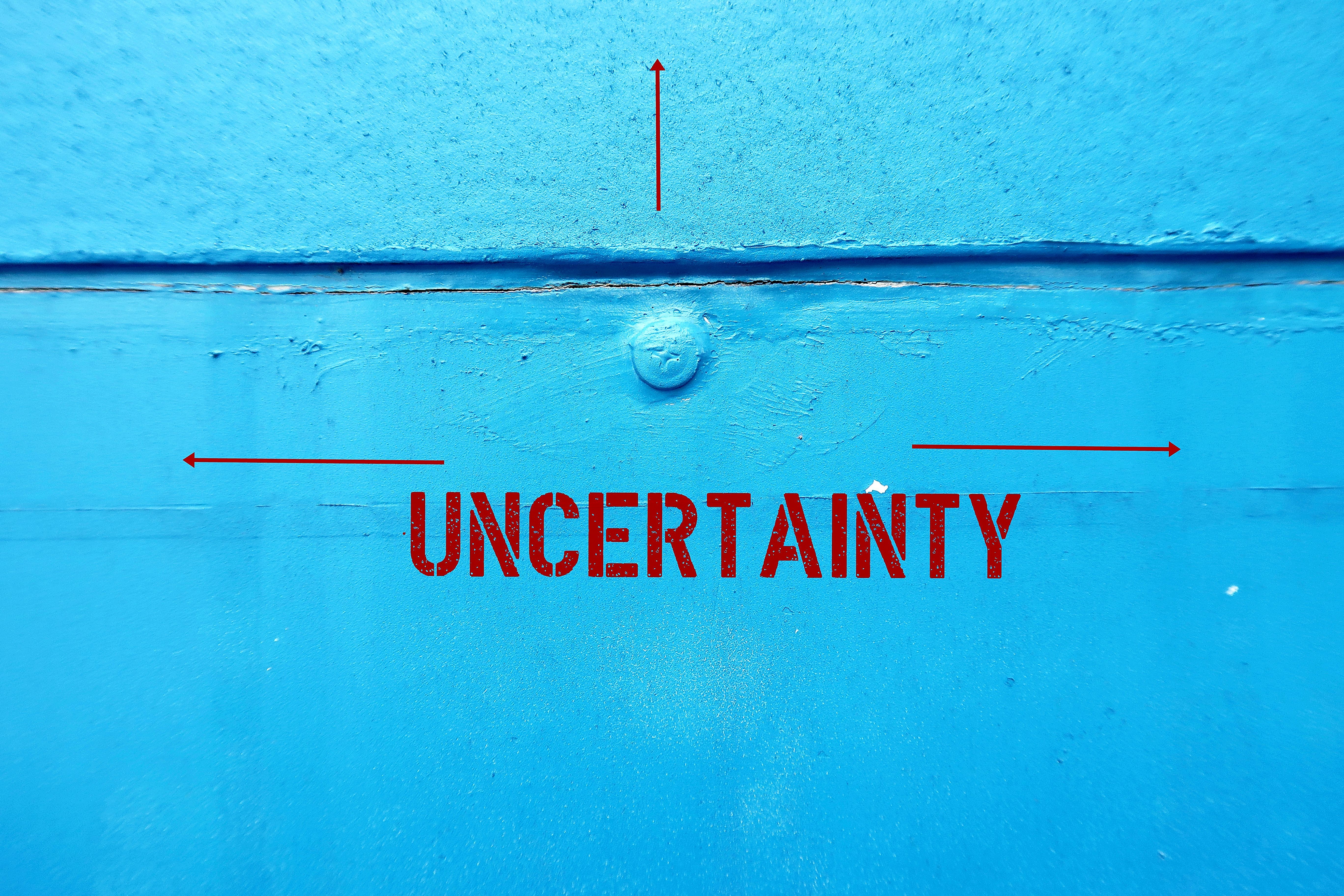 Blue painting wall with text and multi - directions to UNCERTAINTY, means lacking of certainty or sureness of event, struggling to survive in age of uncertainty after pandemic Blue painting wall with text and multi - directions to UNCERTAINTY, means lacking of certainty or sureness of event, struggling to survive in age of uncertainty after pandemic