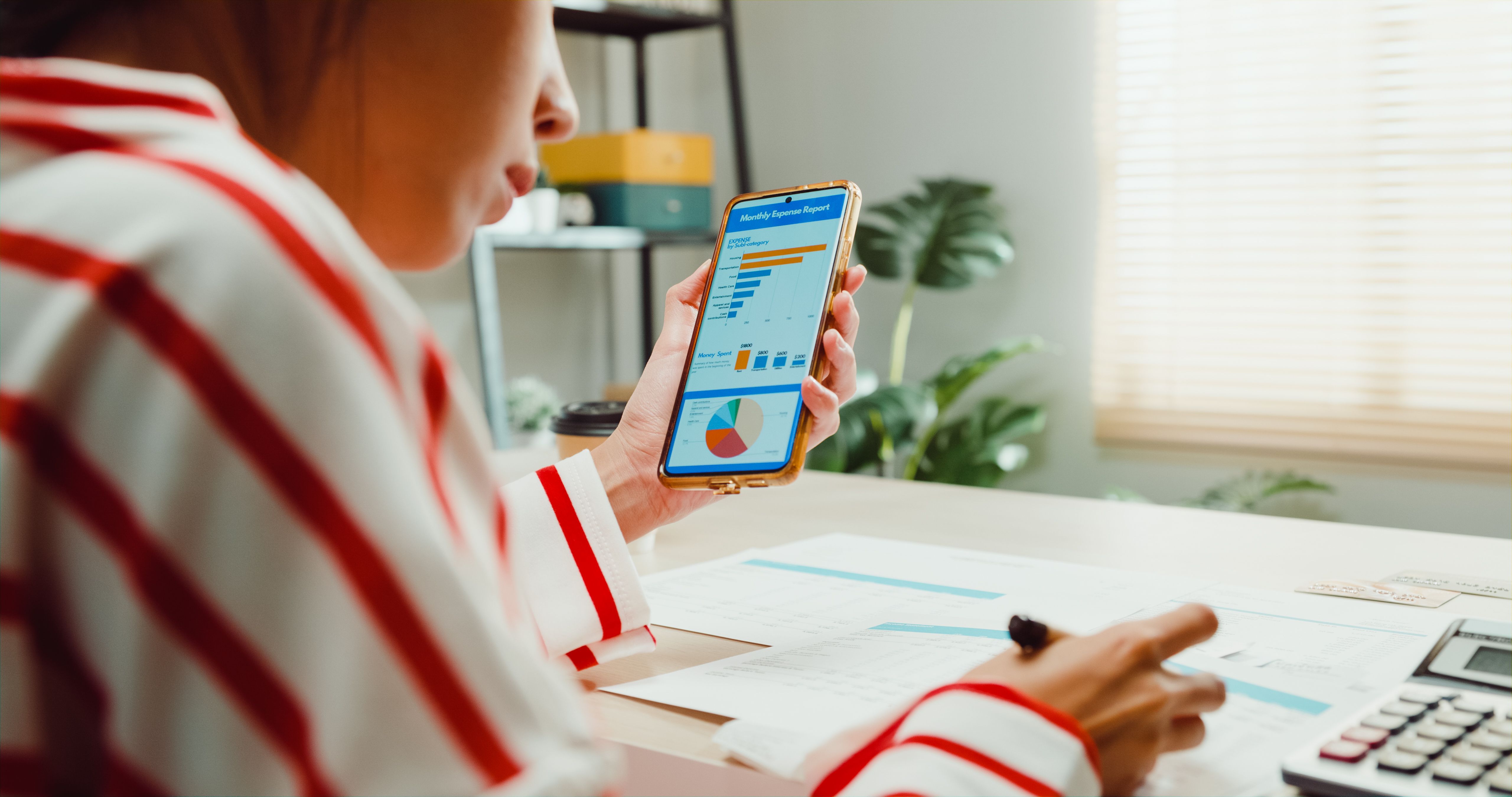 Close-up Young Asian woman with sweater sit front desk with calculator check utility bills, credit card receipt expense bill with monthly financial data in smartphone at home.