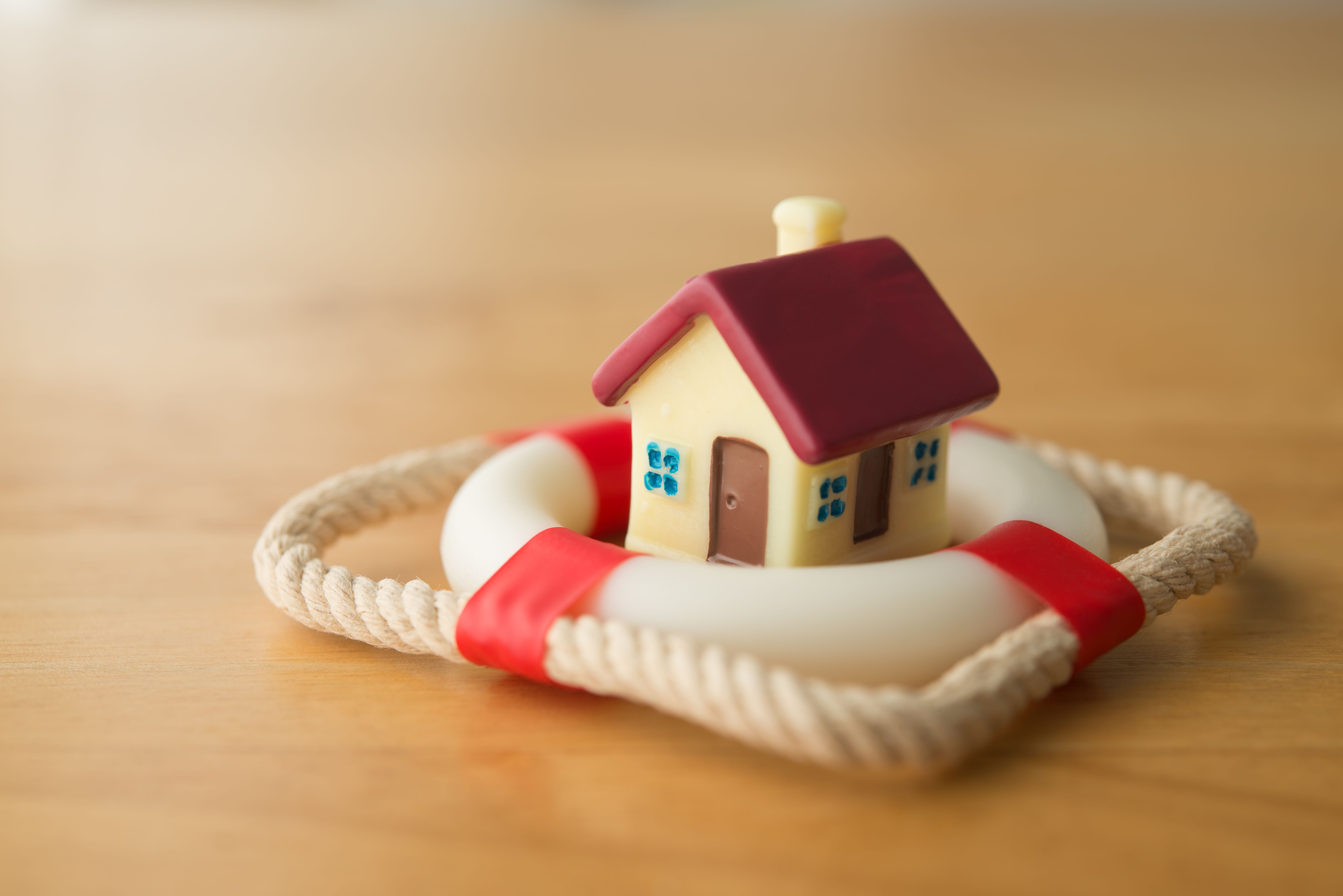 Cute house model is in lifebuoy on wooden table background. Cute house model is in lifebuoy on wooden table background.