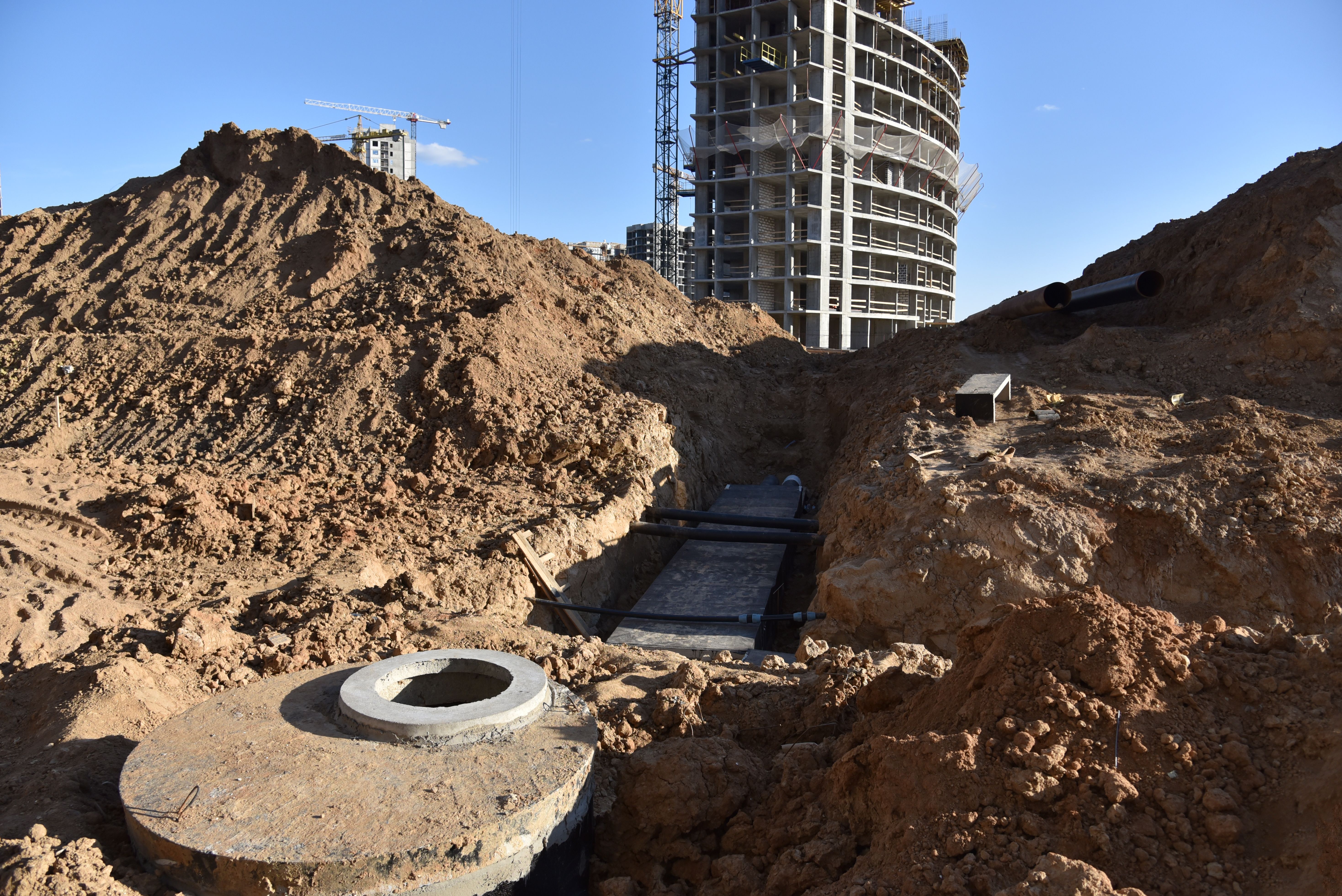 Laying concrete manholes and heating drain pipes and for stormwater system in trench at construction site. Sewerage manhole and pipes line under construction. Chambers and Pump Station Laying concrete manholes and heating drain pipes and for stormwater system in trench at construction site. Sewerage manhole and pipes line under construction. Chambers and Pump Station