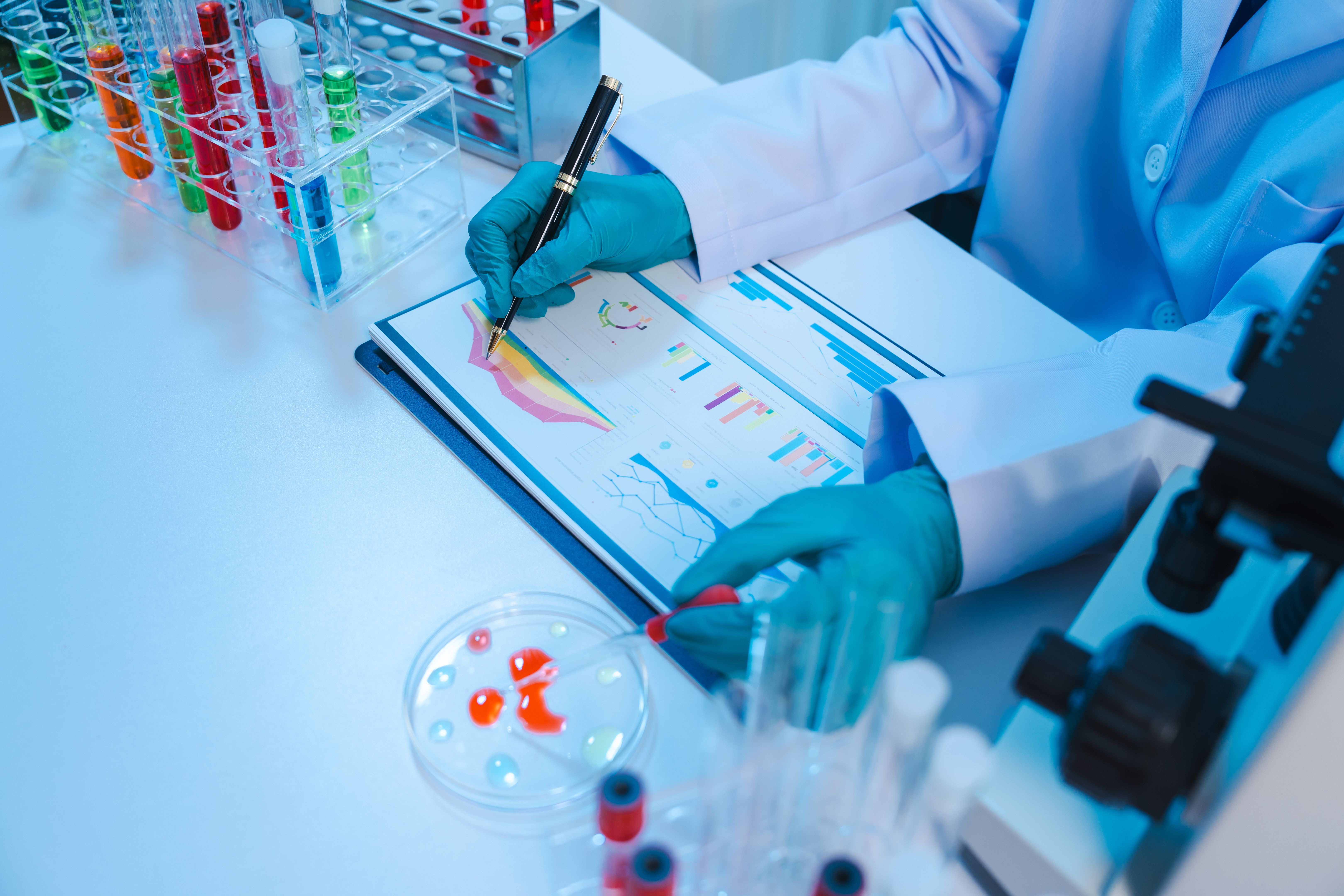 Asian people scientist in lab coat and protective gloves working with test tubes with green and red liquids, with microscope and other test tubes in the background in laboratory.