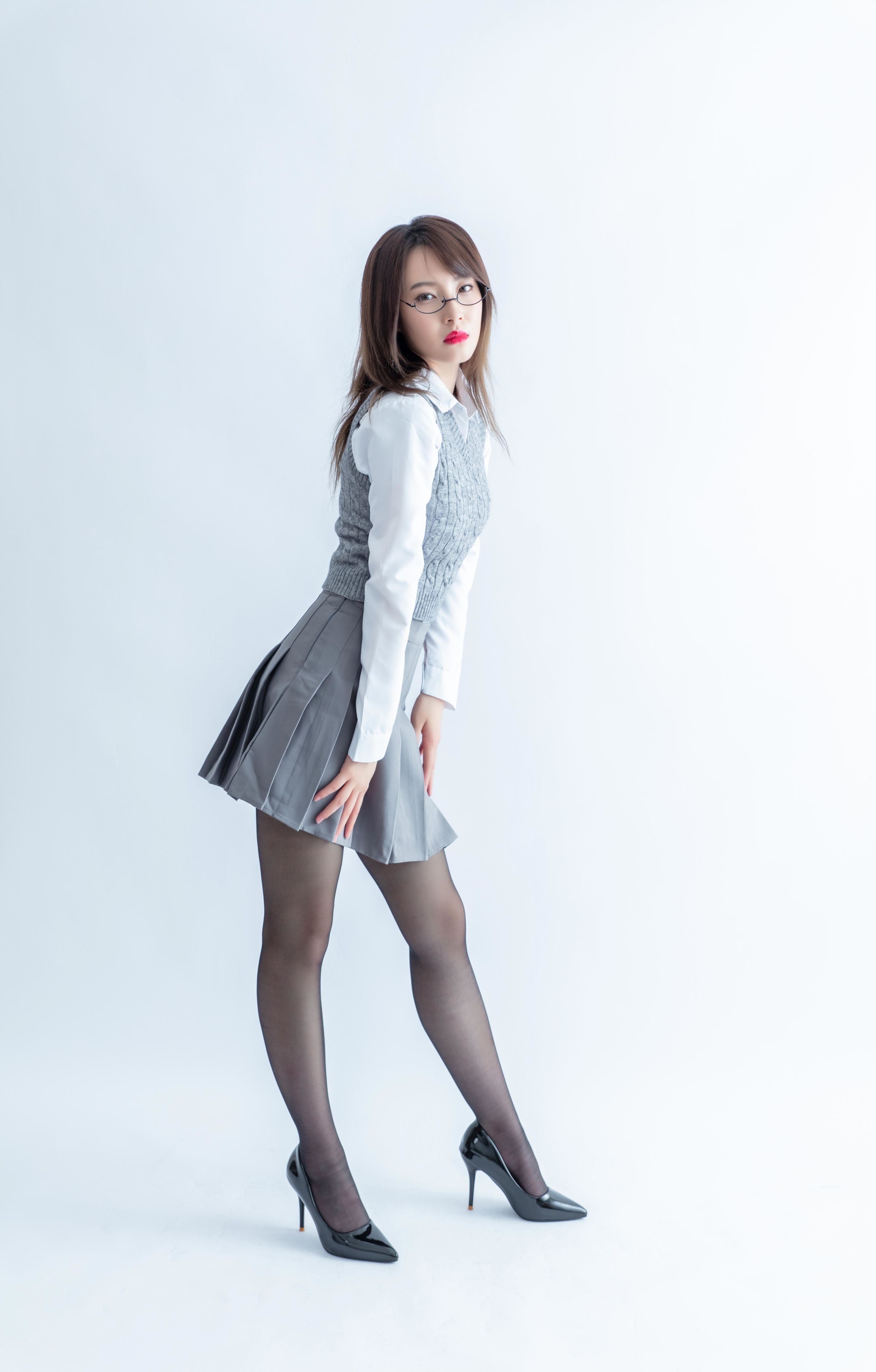 Elegant young Asian school girl in gray pleated skirt and white blouse posing