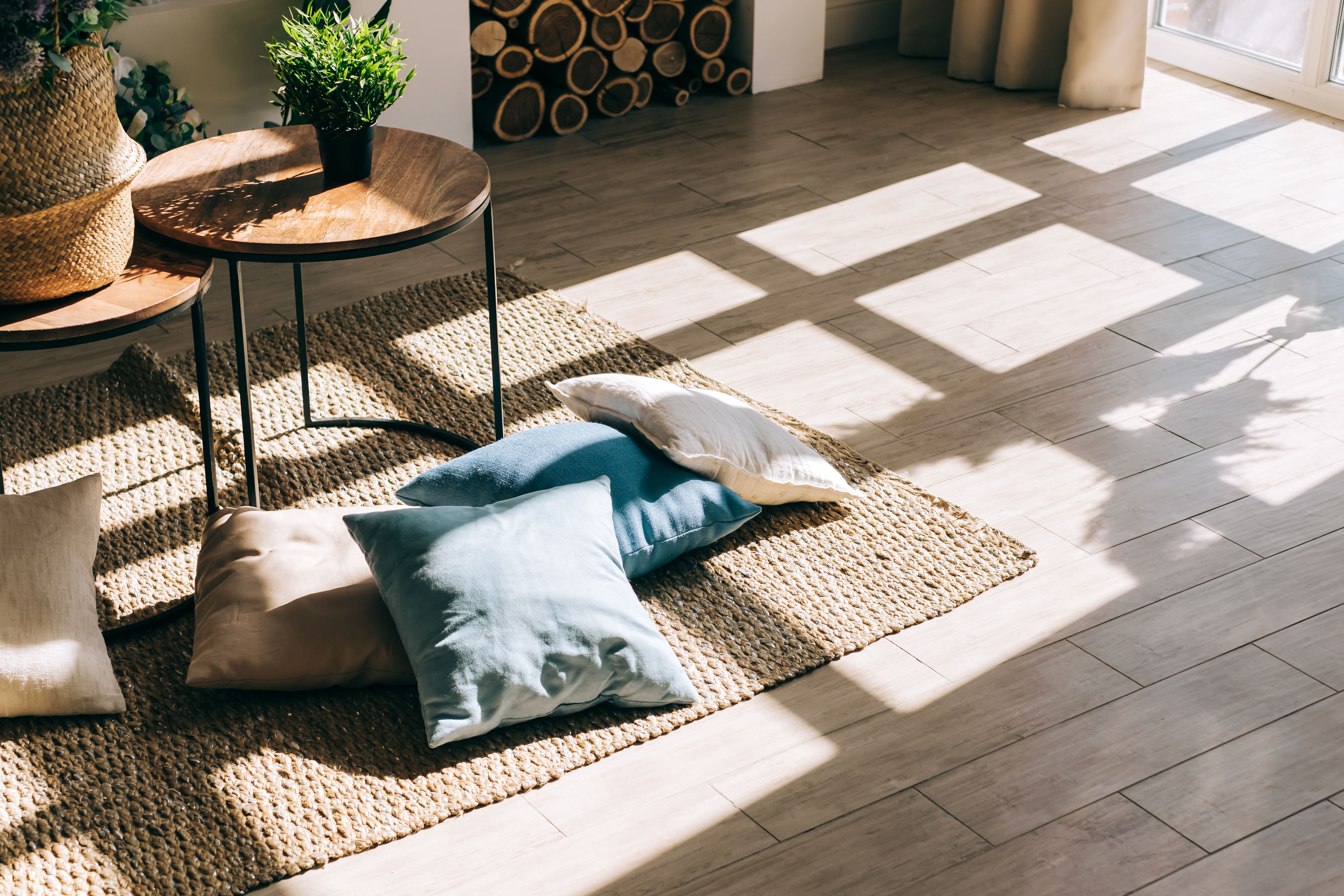 Interior of bright living room in scandinavian style with coffee table and pillows on the floor, big shadow from window on the floor. Interior of bright living room in scandinavian style with coffee table and pillows on the floor, big shadow from window on the floor.