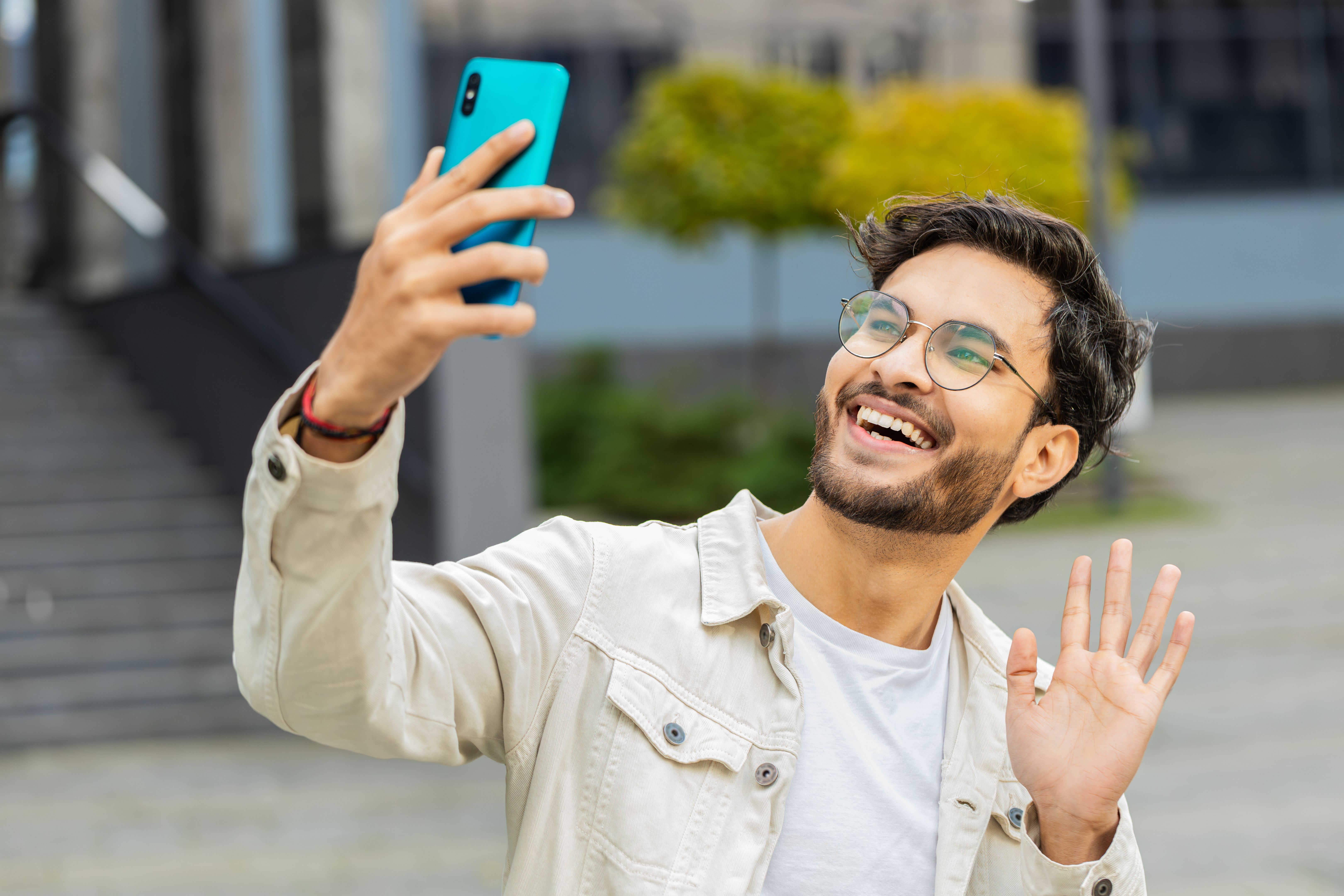 Indian man blogger taking selfie on smartphone video call online with subscribers in city street