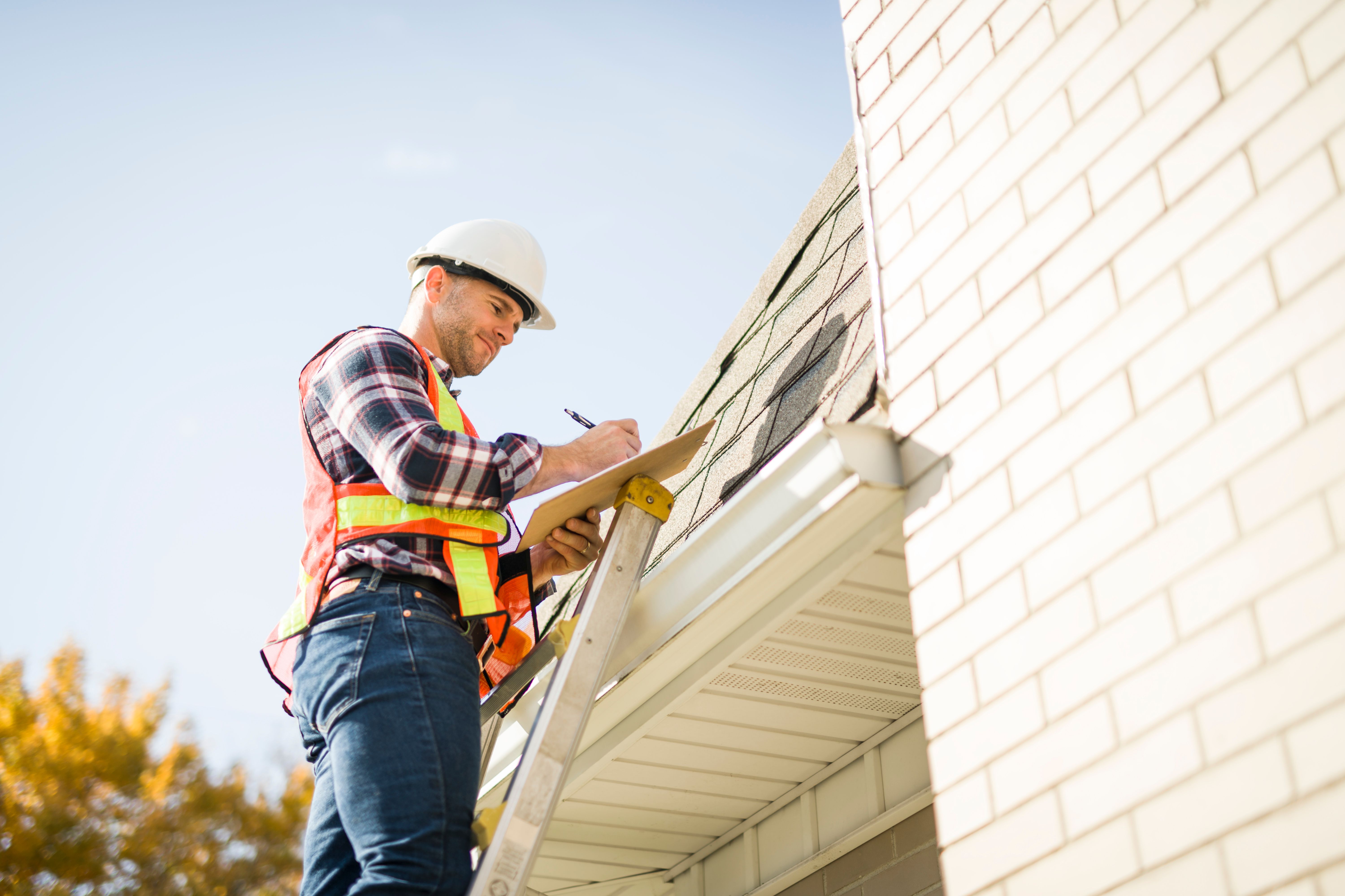 man with hard hat standing on steps inspecting house roof man with hard hat standing on steps inspecting house roof