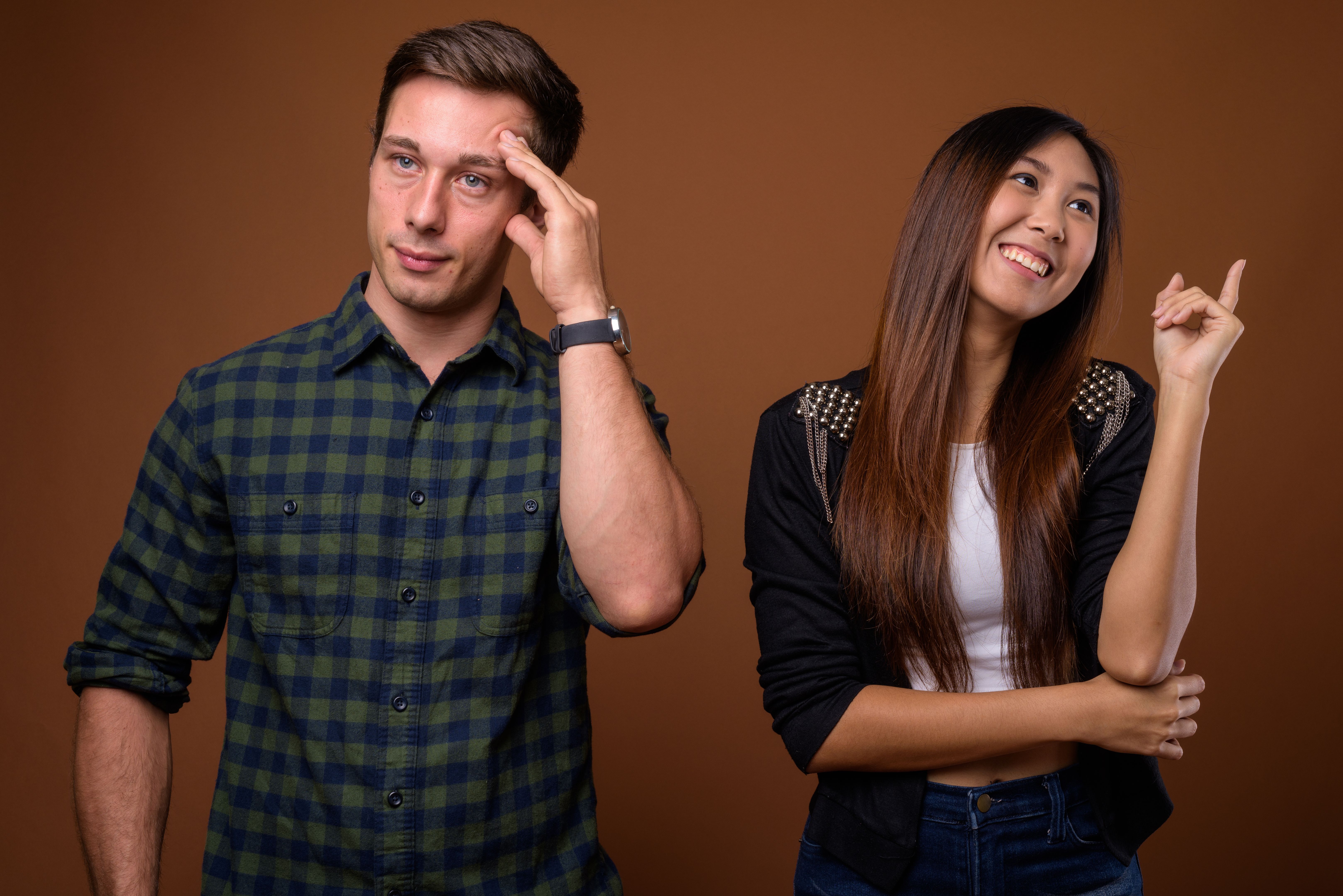 Studio shot of young handsome man and young beautiful Asian woman together against colored background Studio shot of young handsome man and young beautiful Asian woman together against colored background