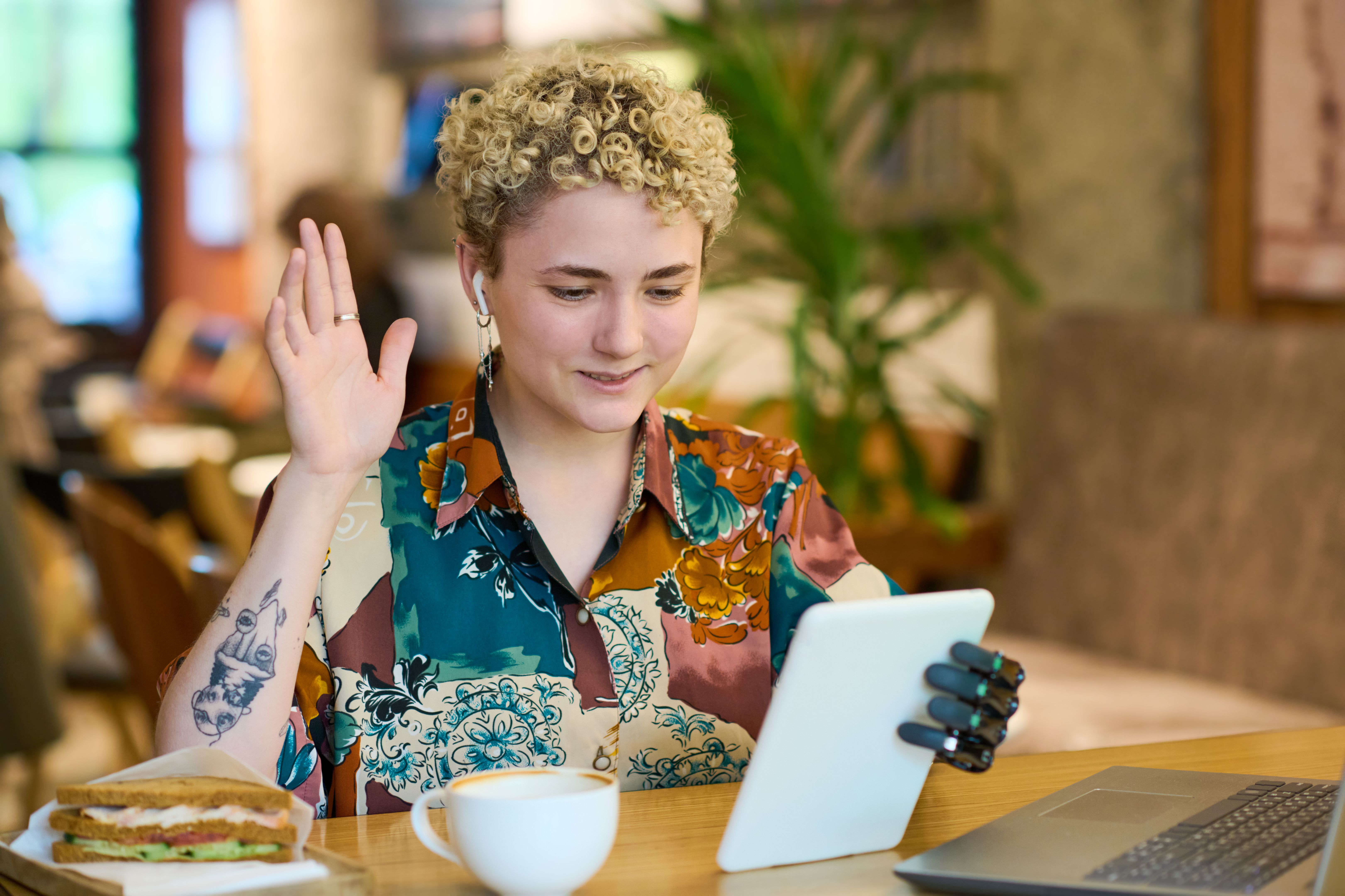 Young smiling woman with disability communicating in video chat in cafe