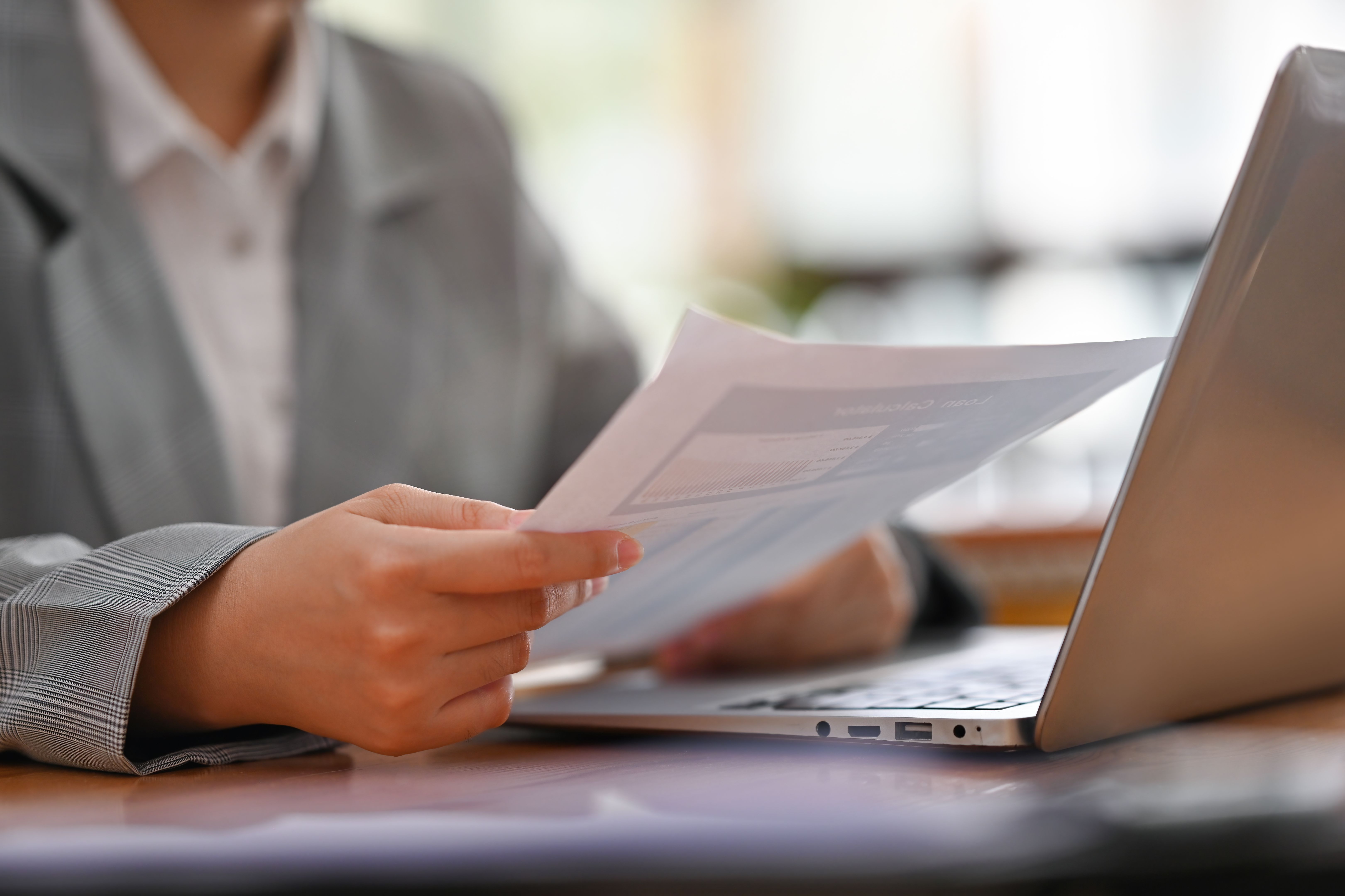 Close up and cropped image of Young businesswoman's hand holding a financial report documents and using laptop.