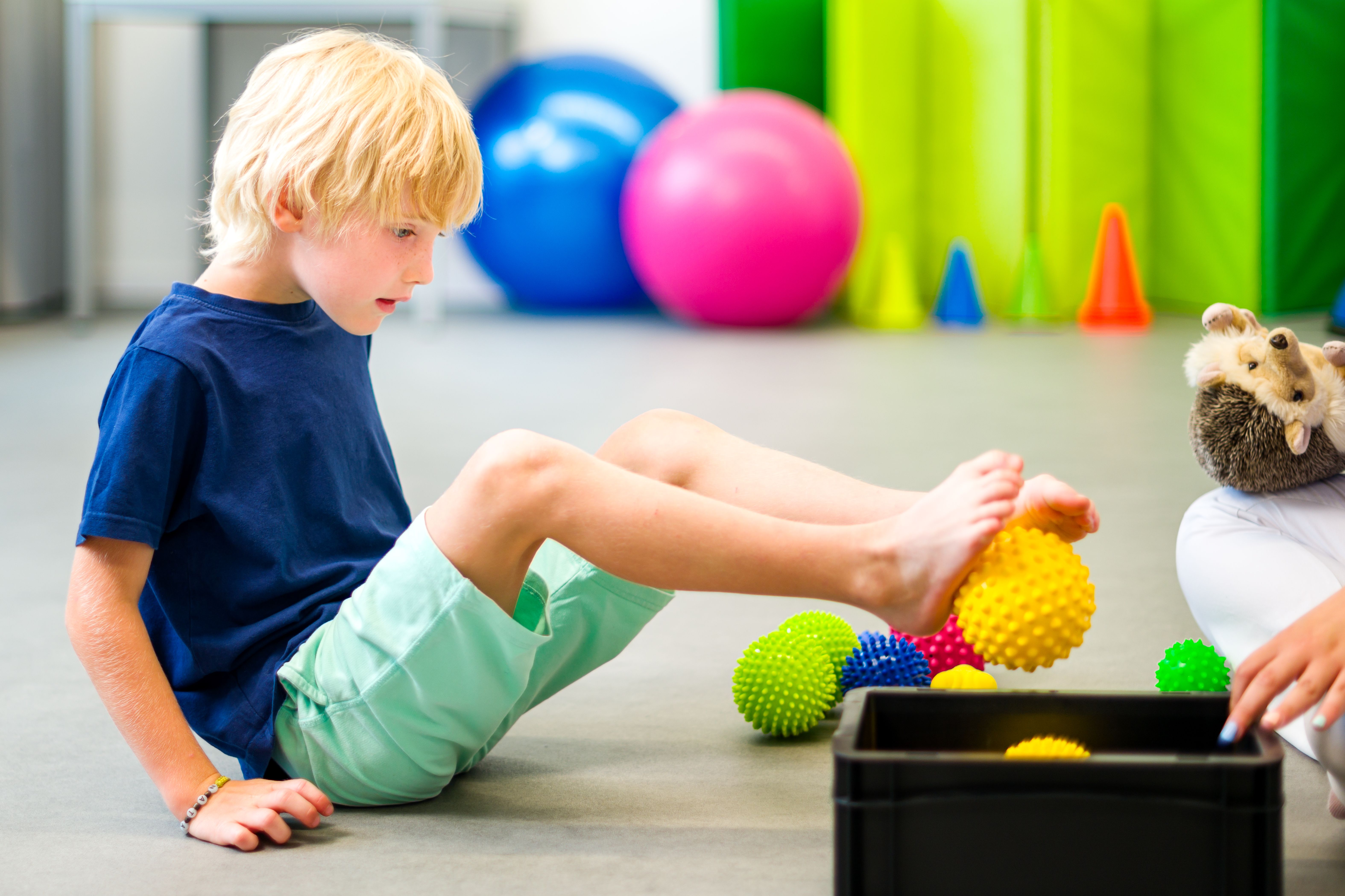 Child during physical therapy session. Boy exercising barefoot with textured surface ball in physio therapy. Flat feet. Child during physical therapy session. Boy exercising barefoot with textured surface ball in physio therapy. Flat feet.