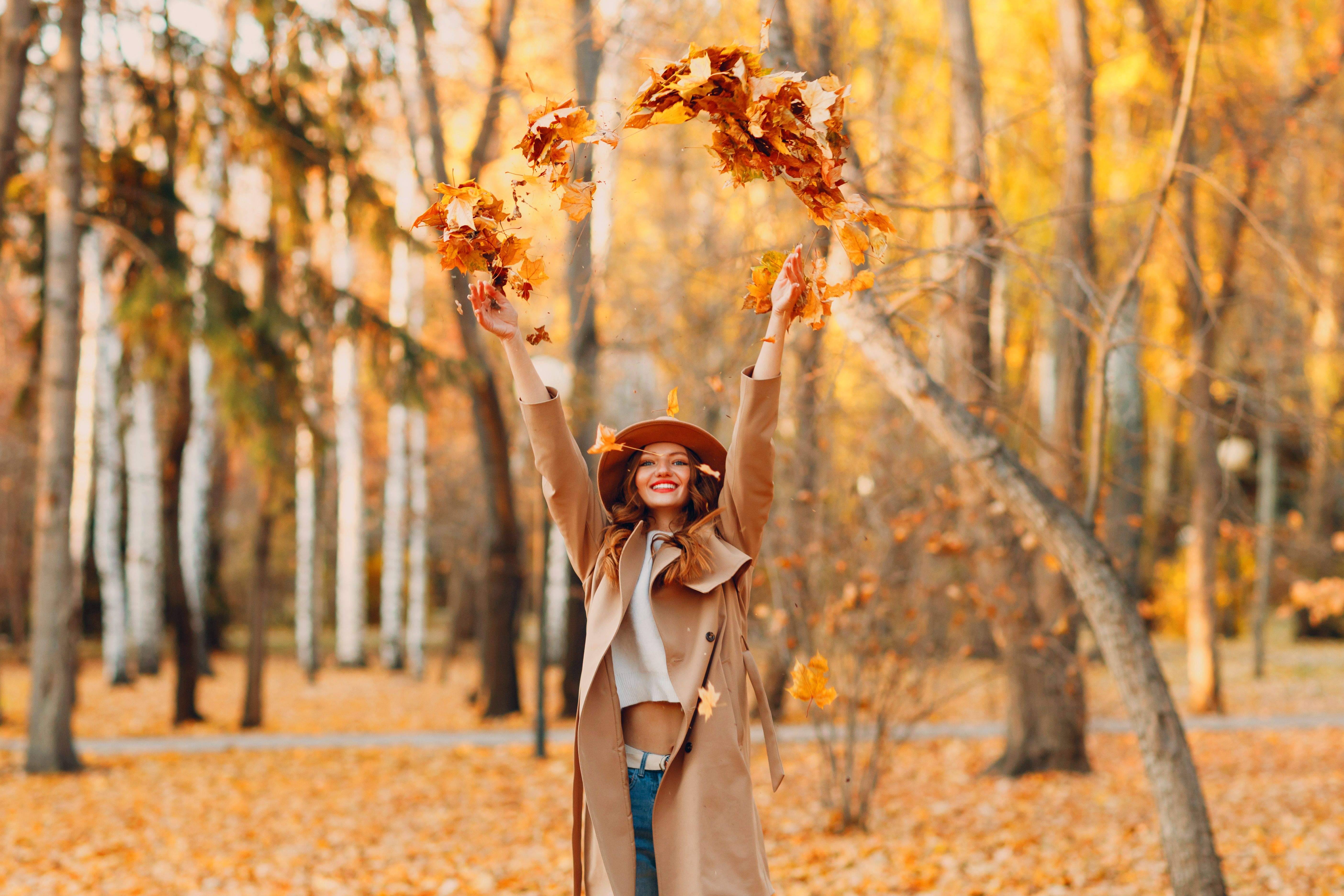 Girl in beautiful autumn park throw up orange leaves. Fall autumn season fashion.