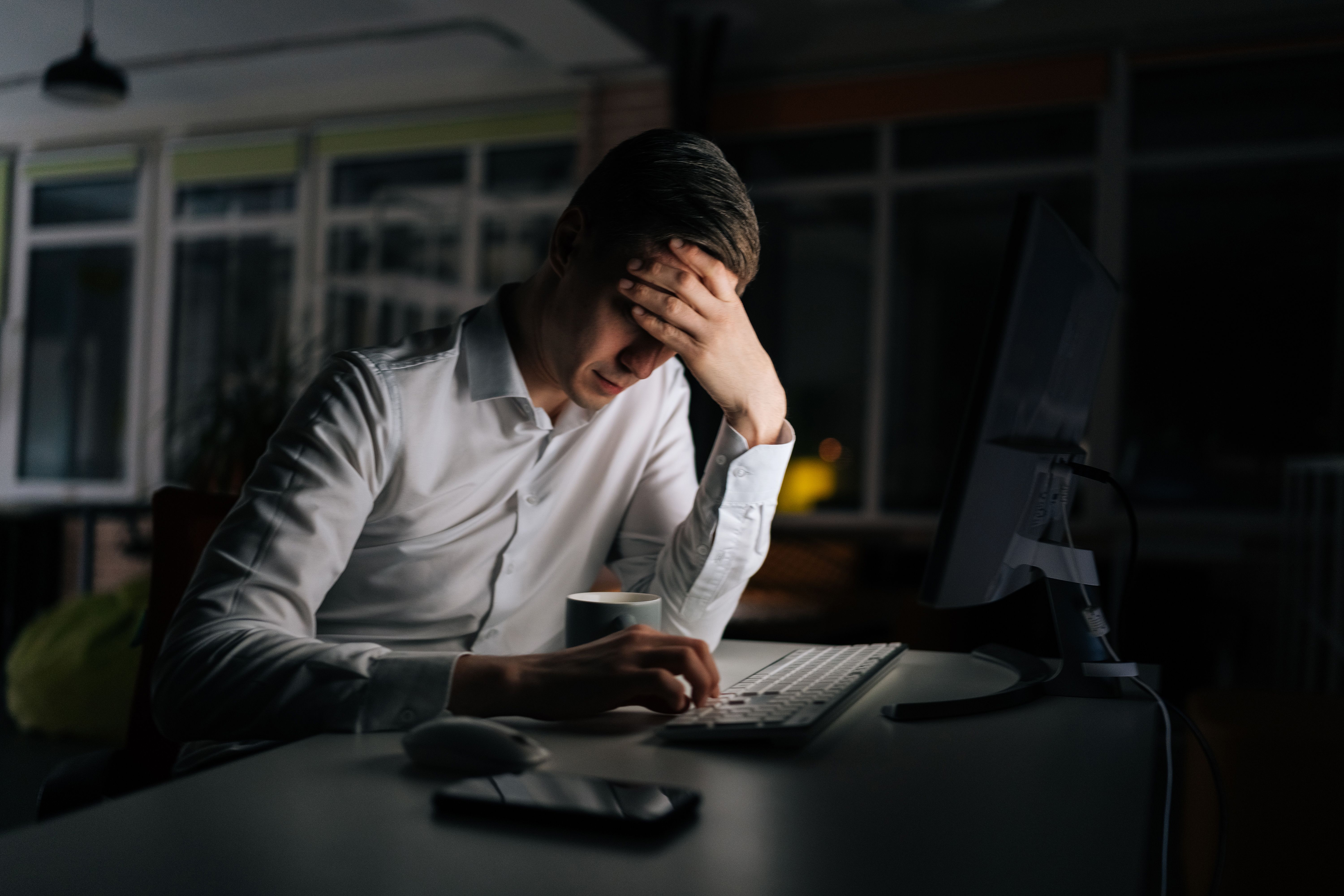 Exhausted businessman working in evening office alone. Tired anxious manager losing failure working on computer at late night. Tired worried business man at workplace