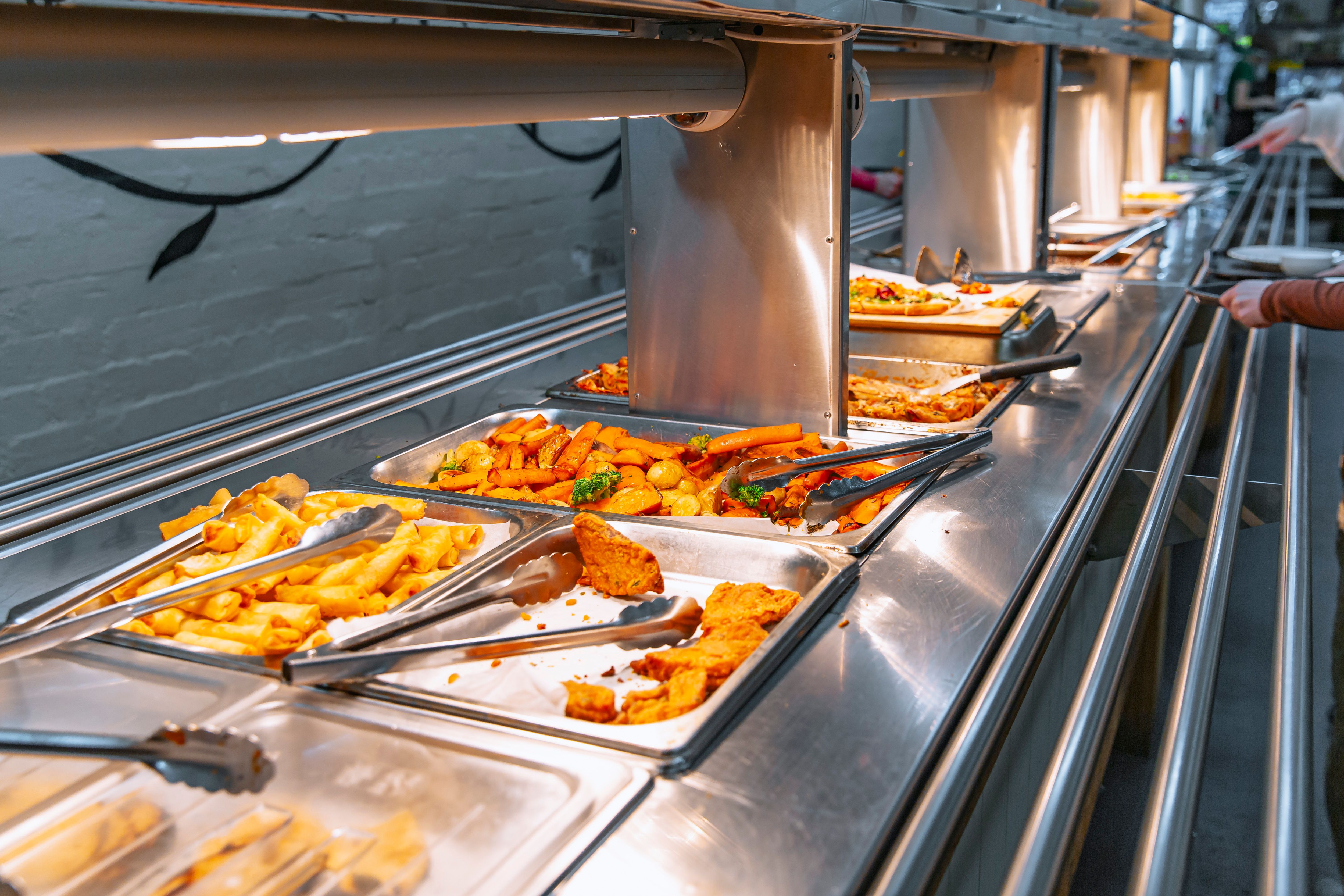 Variety vegetarian dishes metal trays heating lamps cafeteria buffet fried items vegetables lasagna Variety vegetarian dishes metal trays heating lamps cafeteria buffet fried items vegetables lasagna