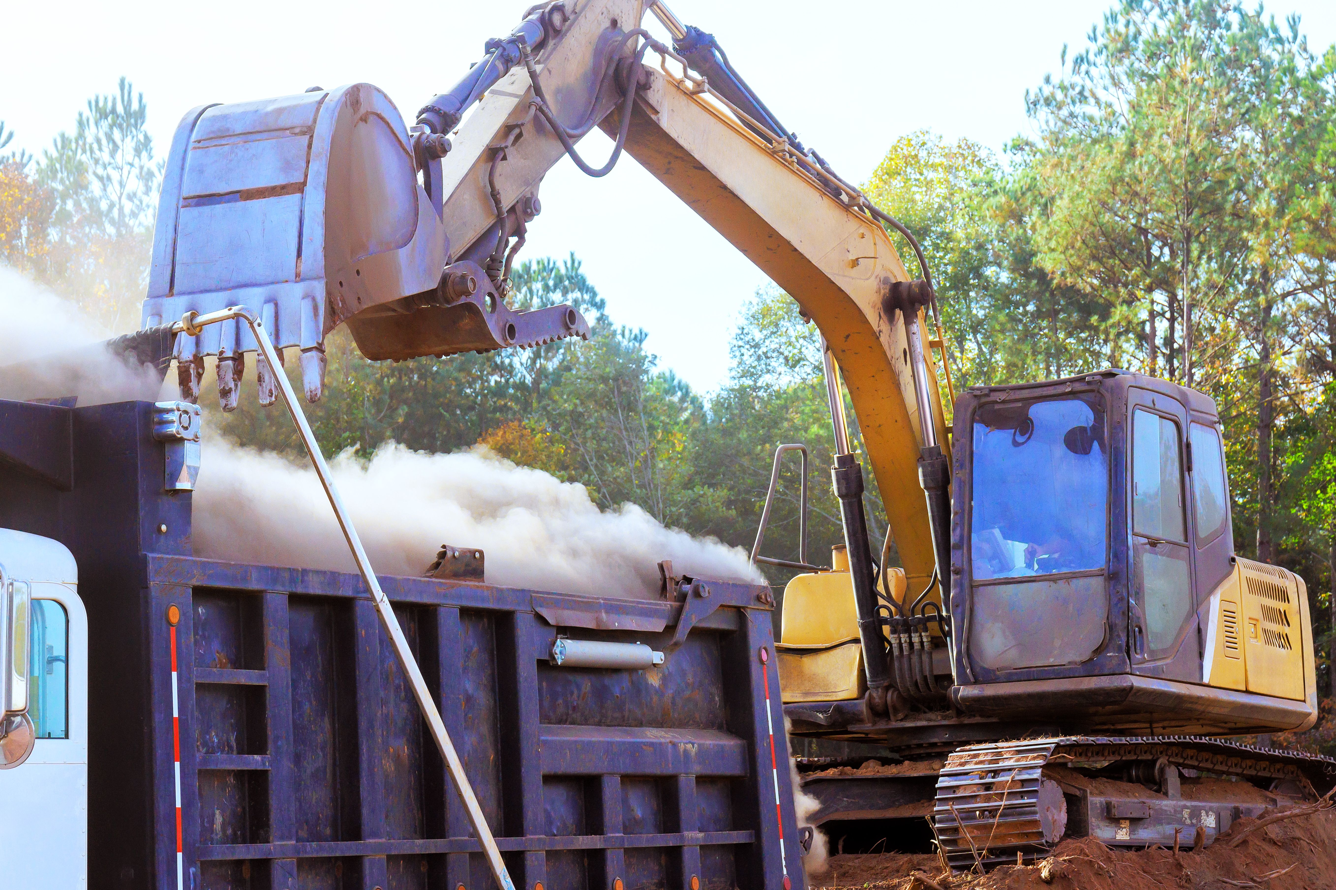 Heavy machinery performs excavation work at construction site with dust debris rising from ground under land removal