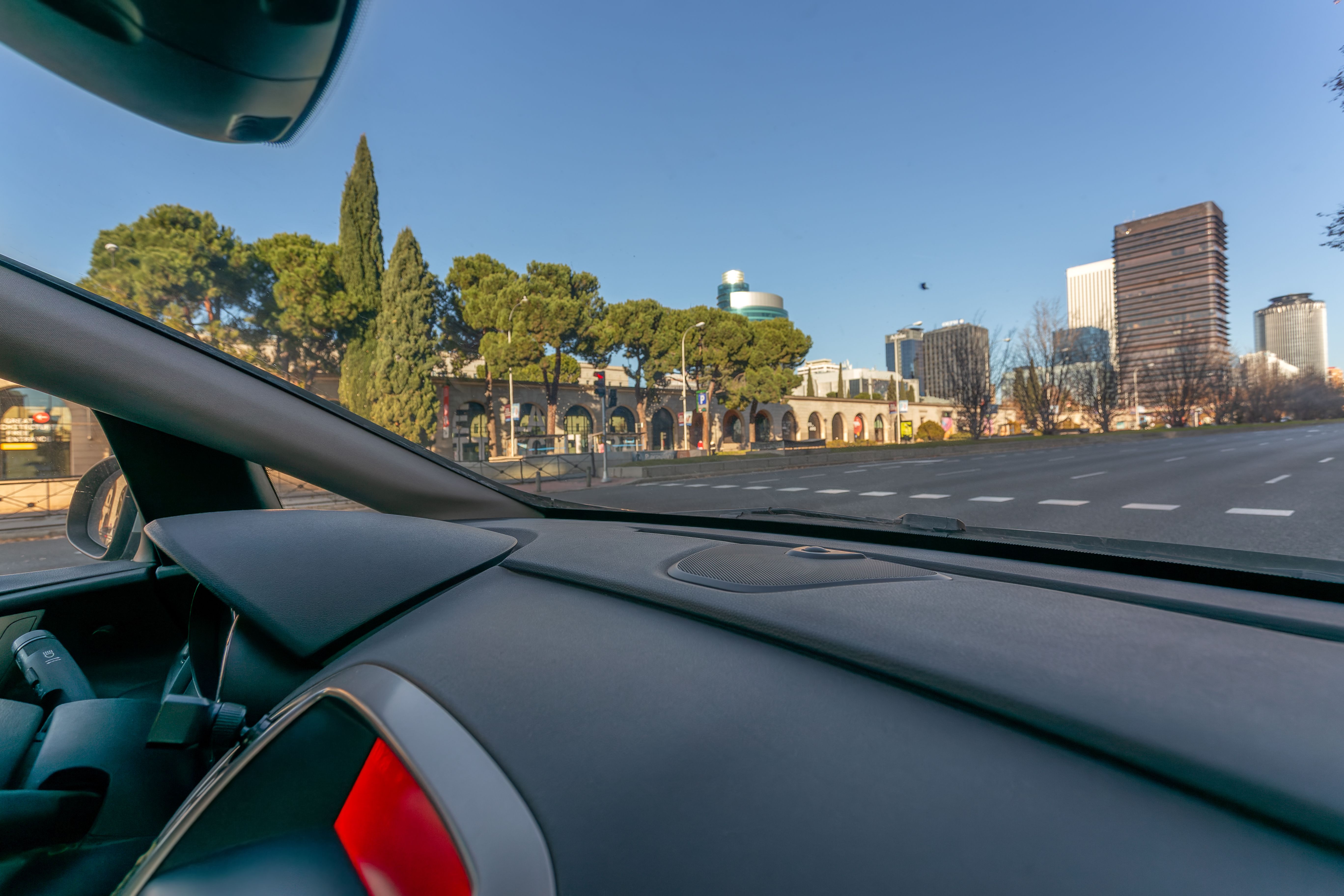 View from inside a vehicle driving along Paseo de la Castellana near Nuevos Ministerios on a sunny morning.