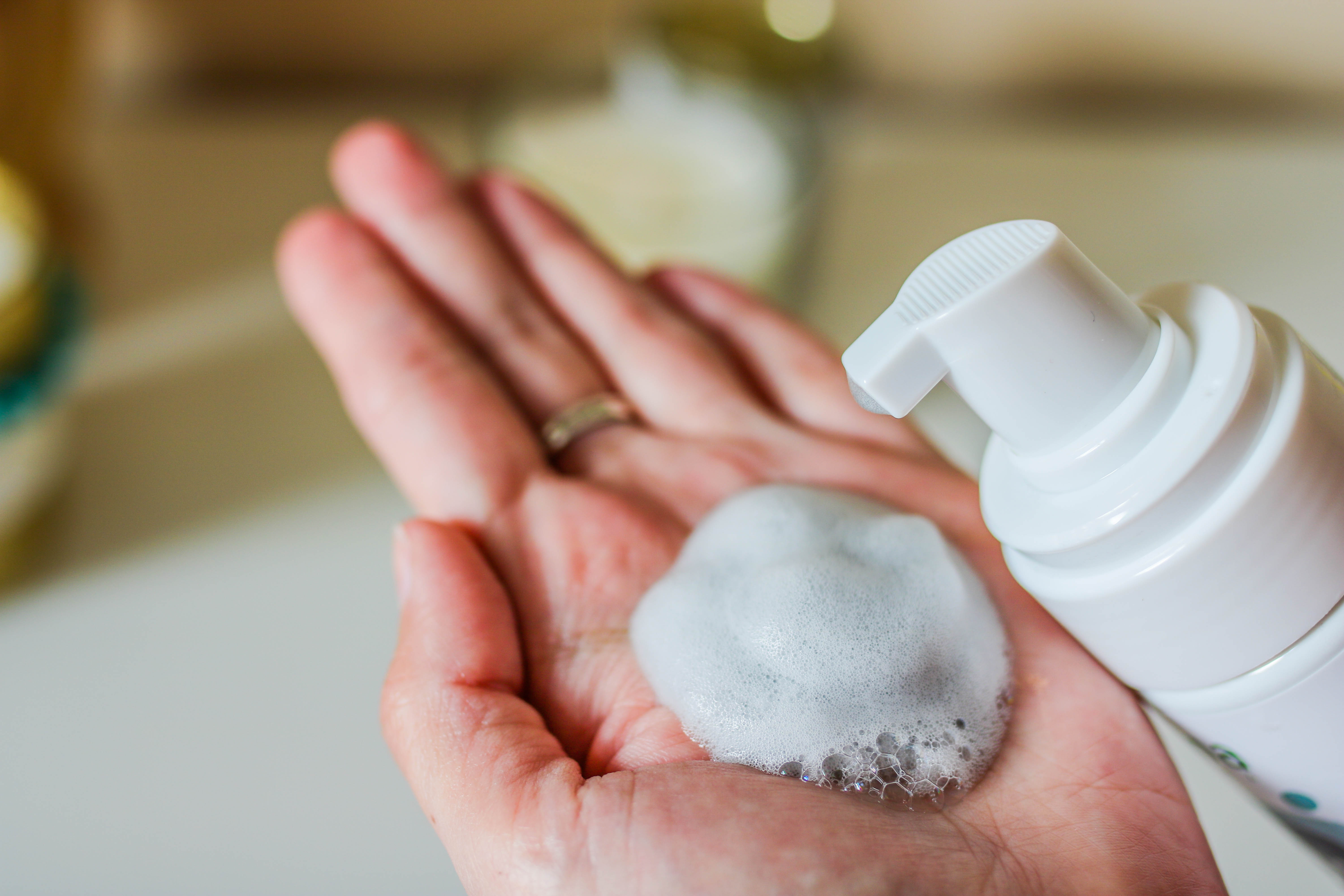 Face cleanser on female hand and cosmetics foam pump container. White blurred background.