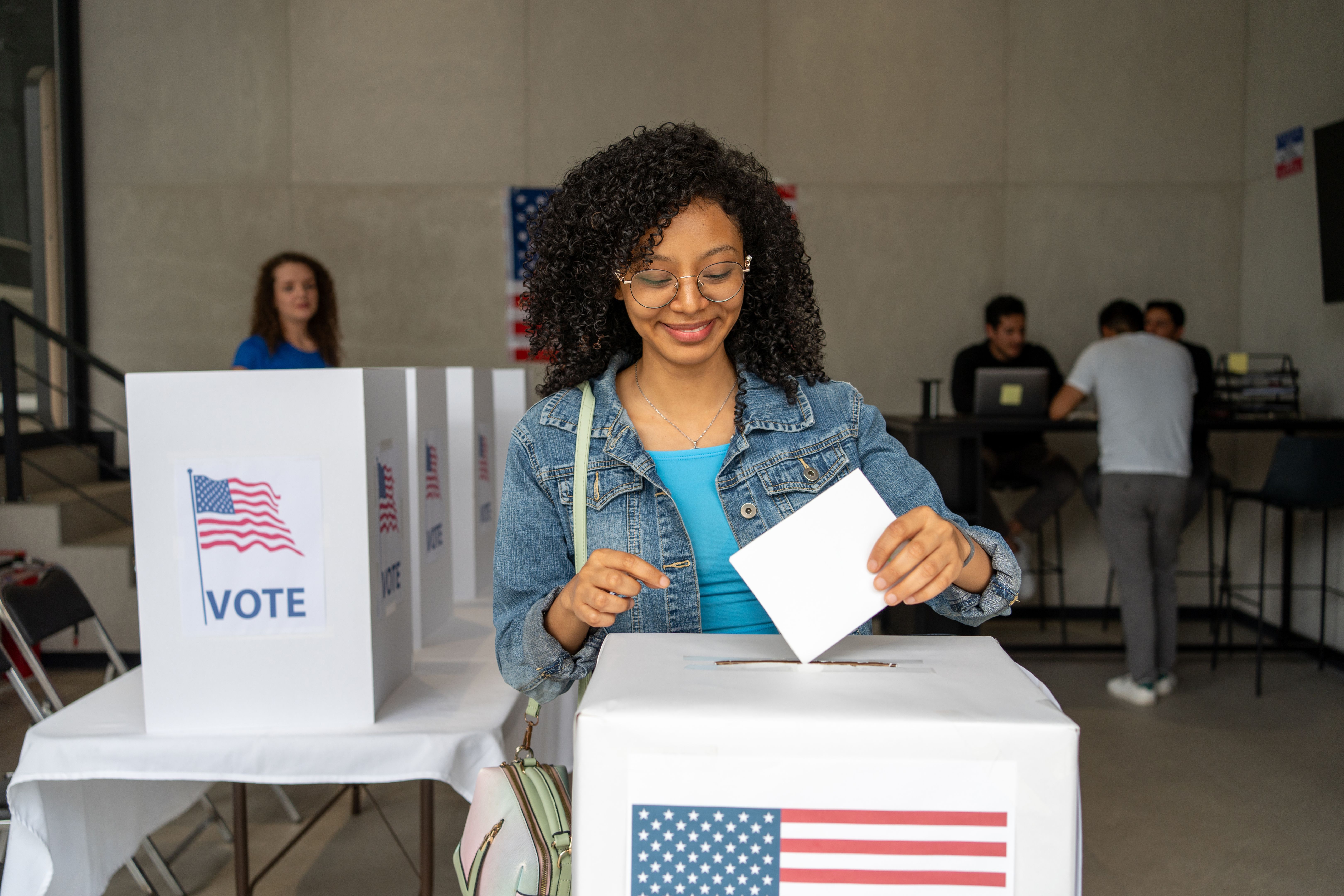 portrait of a young african american woman voting in the us election, placing vote ballot in the polling box, vote in America. Concept of choice, democracy and freedom