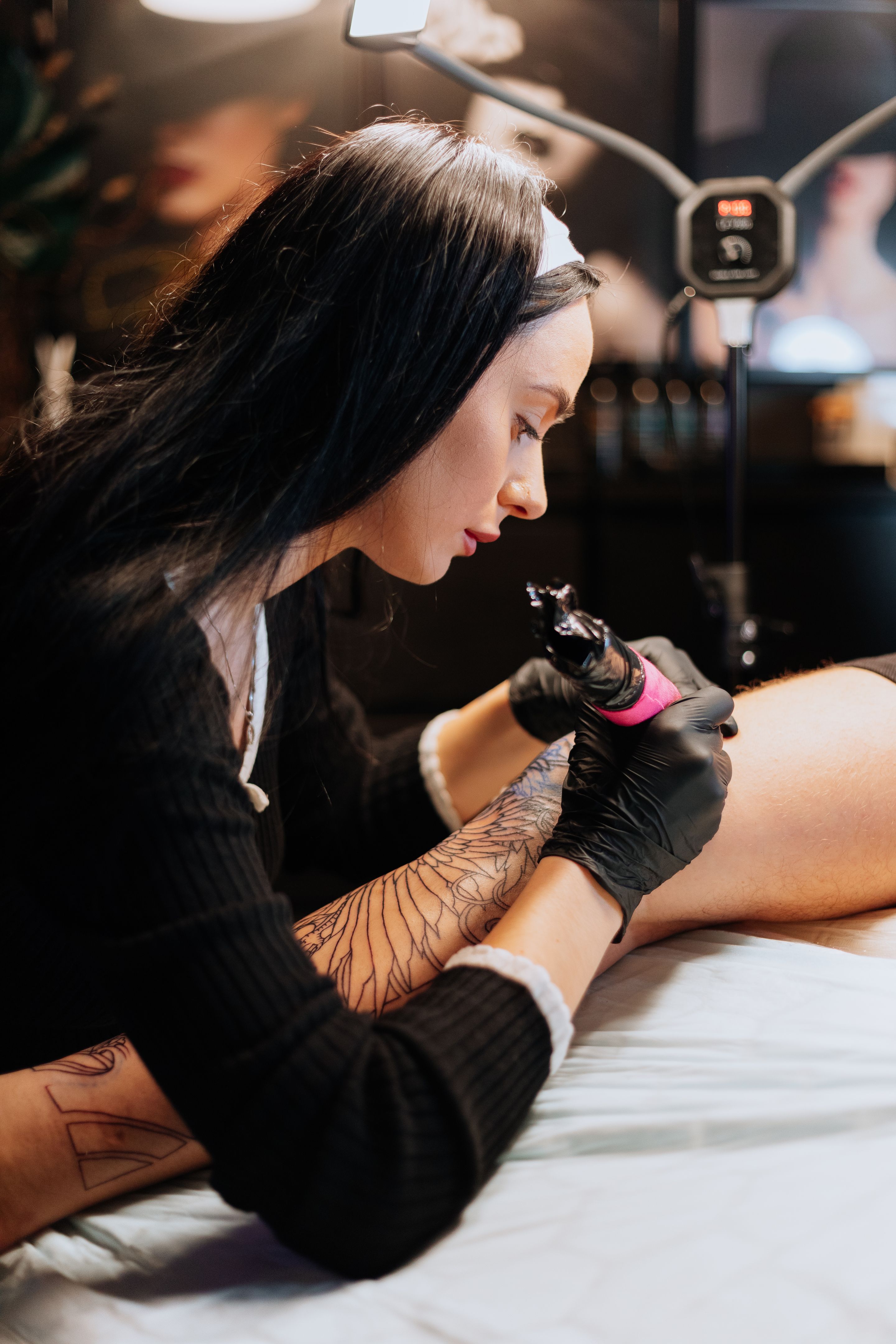 Master tattoo draws tattoo on a man's leg. Tattoo artist holding a pink tattoo machine in black sterile gloves and working. Master tattoo draws tattoo on a man's leg. Tattoo artist holding a pink tattoo machine in black sterile gloves and working.