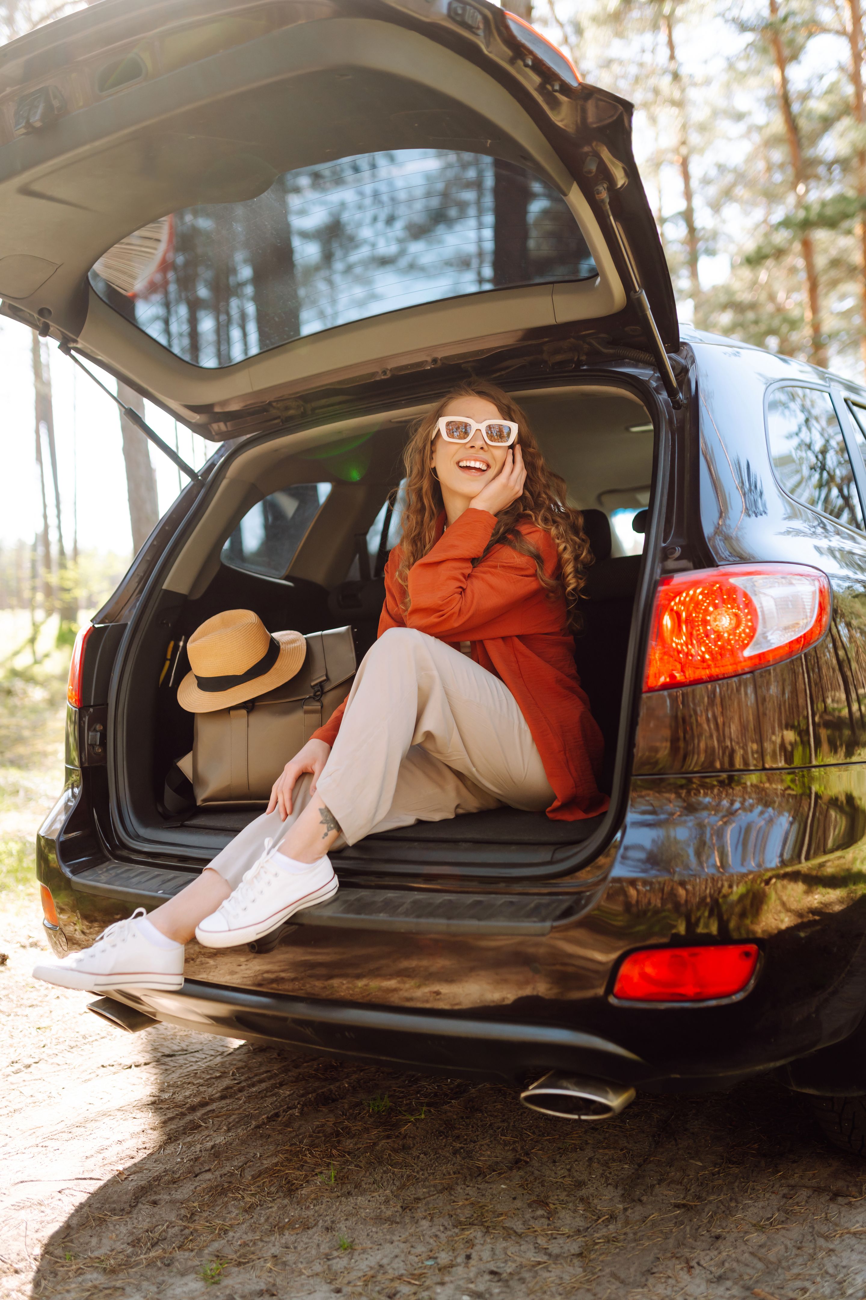 Happy woman enjoying nature while sitting in the trunk of her car during a solo trip.