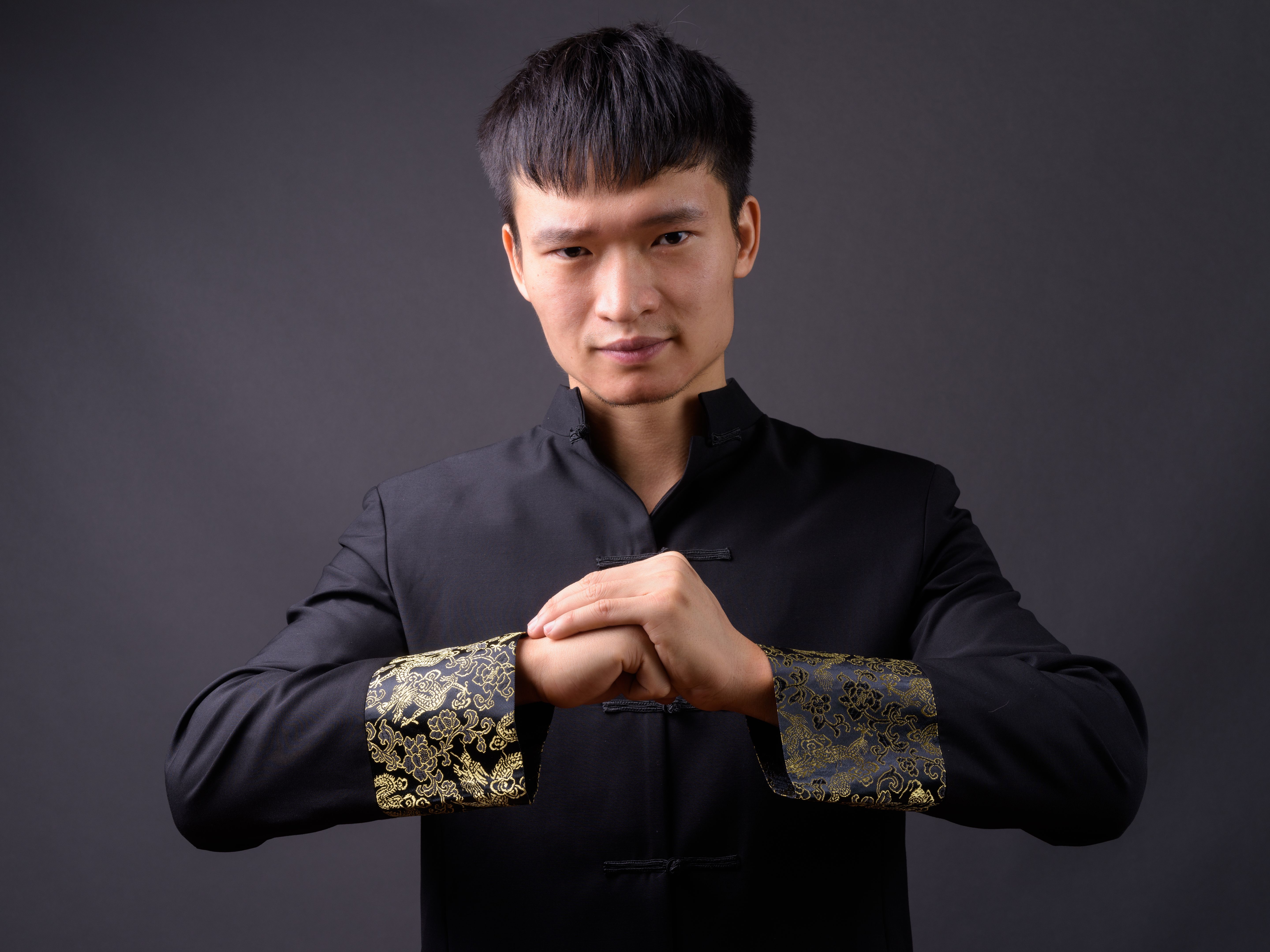 Young Chinese man wearing traditional clothes against gray background