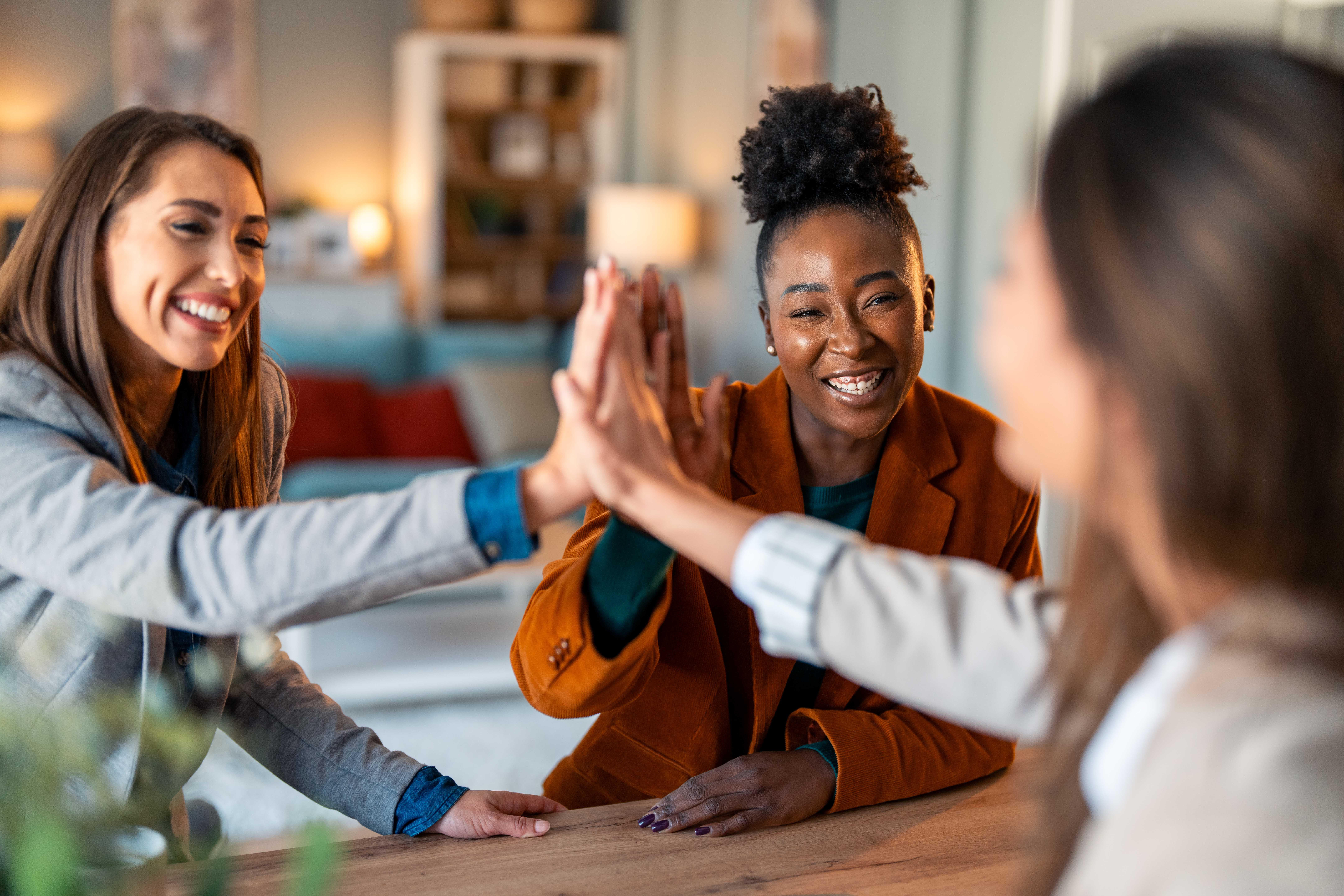Successful businesswomen united as a team high fiving in an office while sitting at the table Successful businesswomen united as a team high fiving in an office while sitting at the table