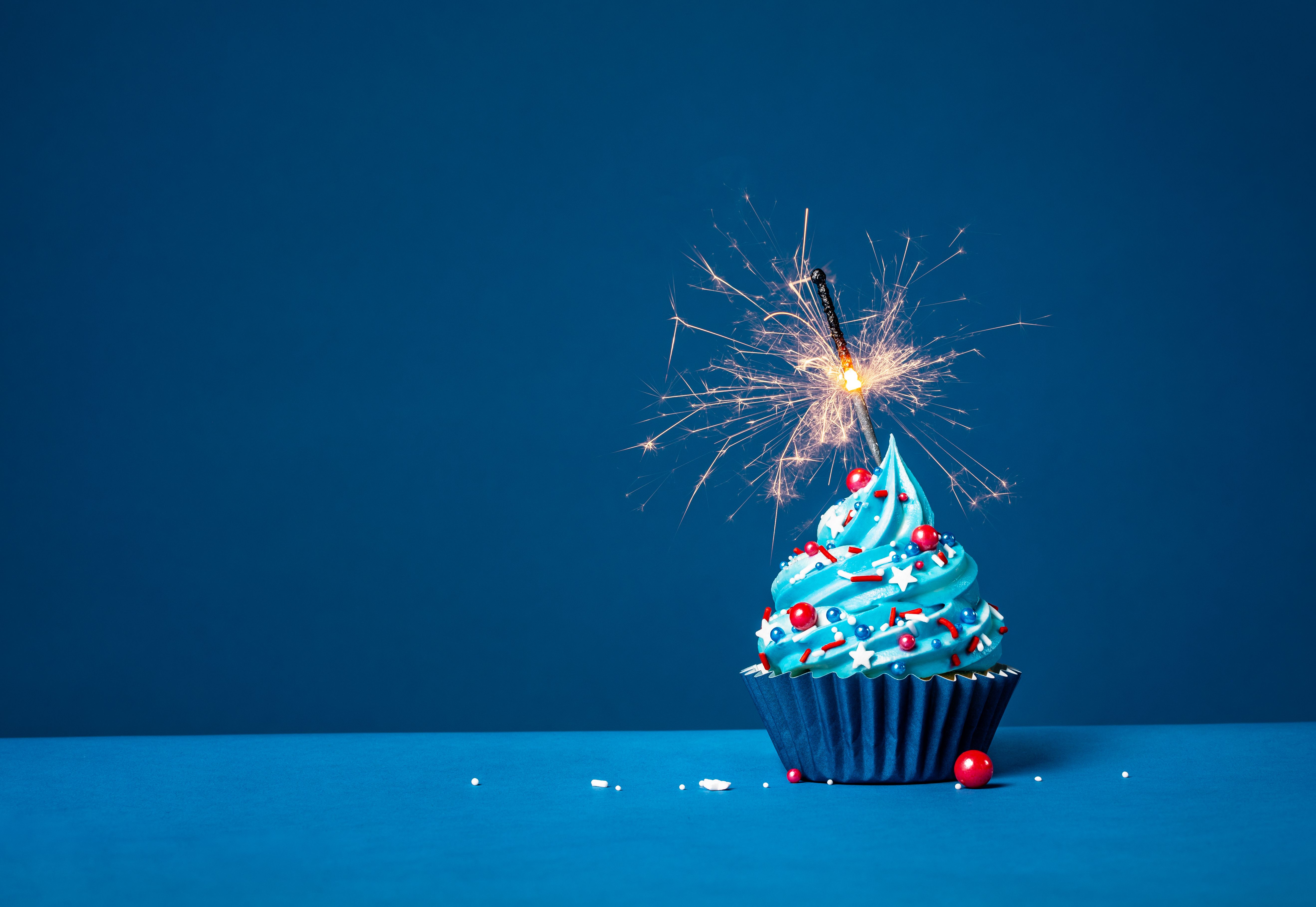 Blue cupcake with red and white sprinkles and lit sparkler on a blue background. Blue cupcake with red and white sprinkles and lit sparkler on a blue background.