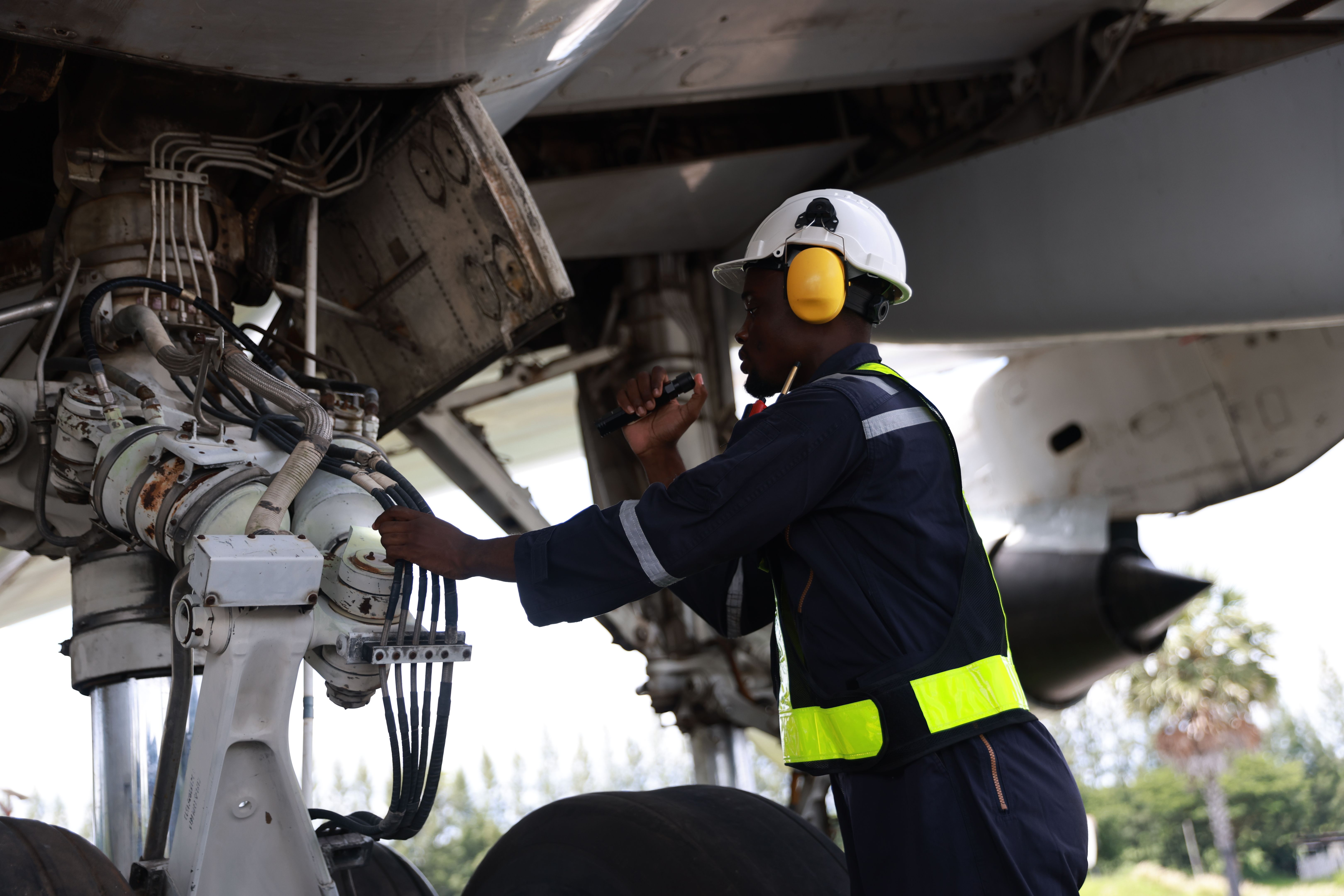 The black male aircraft mechanics use hand tools to work on inspection and do maintenance of an airplane, Aircraft technician examining a plane in the hangar