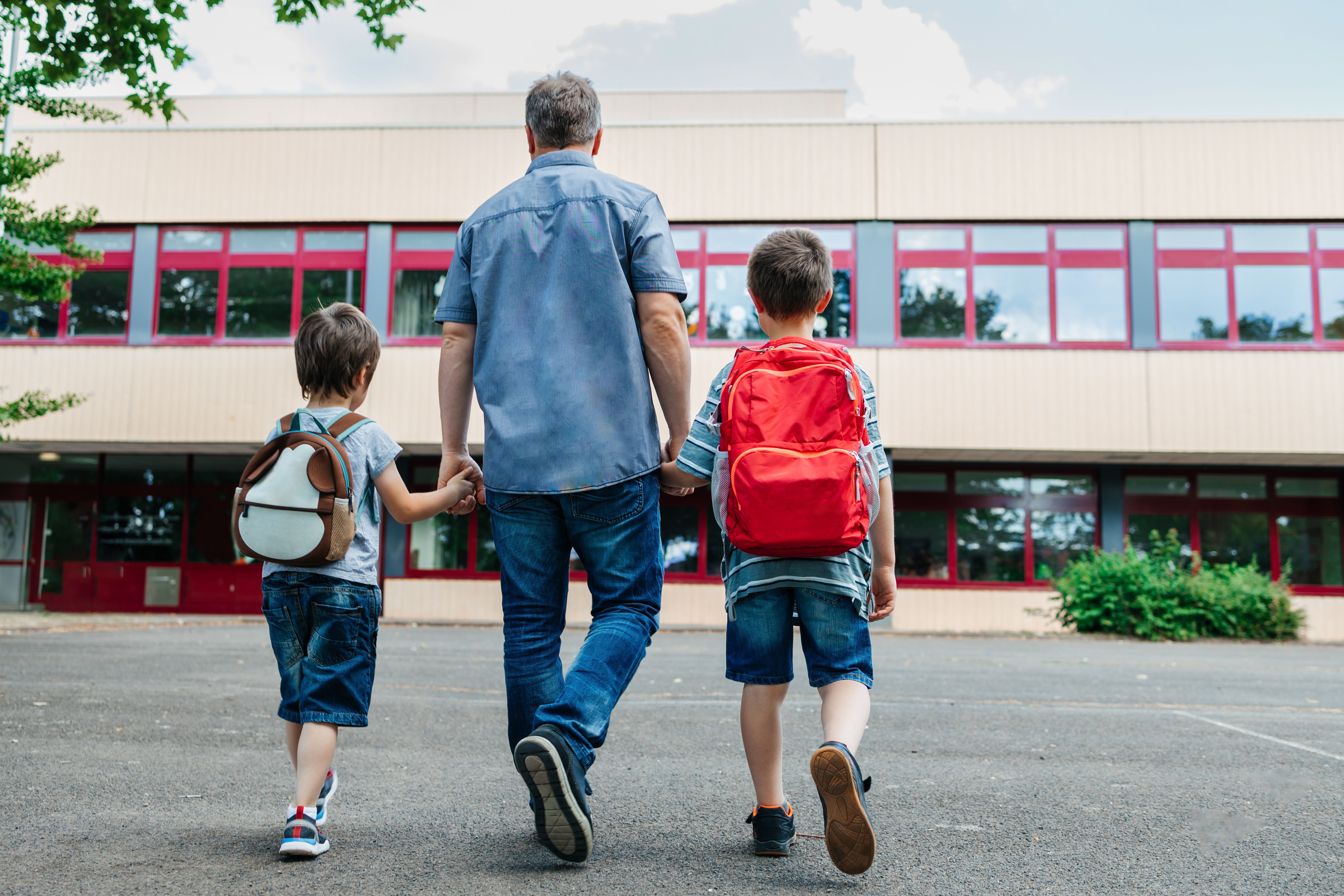 Zurück zur Schule. Blick vom Rücken eines glücklichen Vaters begleitet die Schulkinder seiner Söhne zur Schule. Fürsorge der Eltern für Kinder