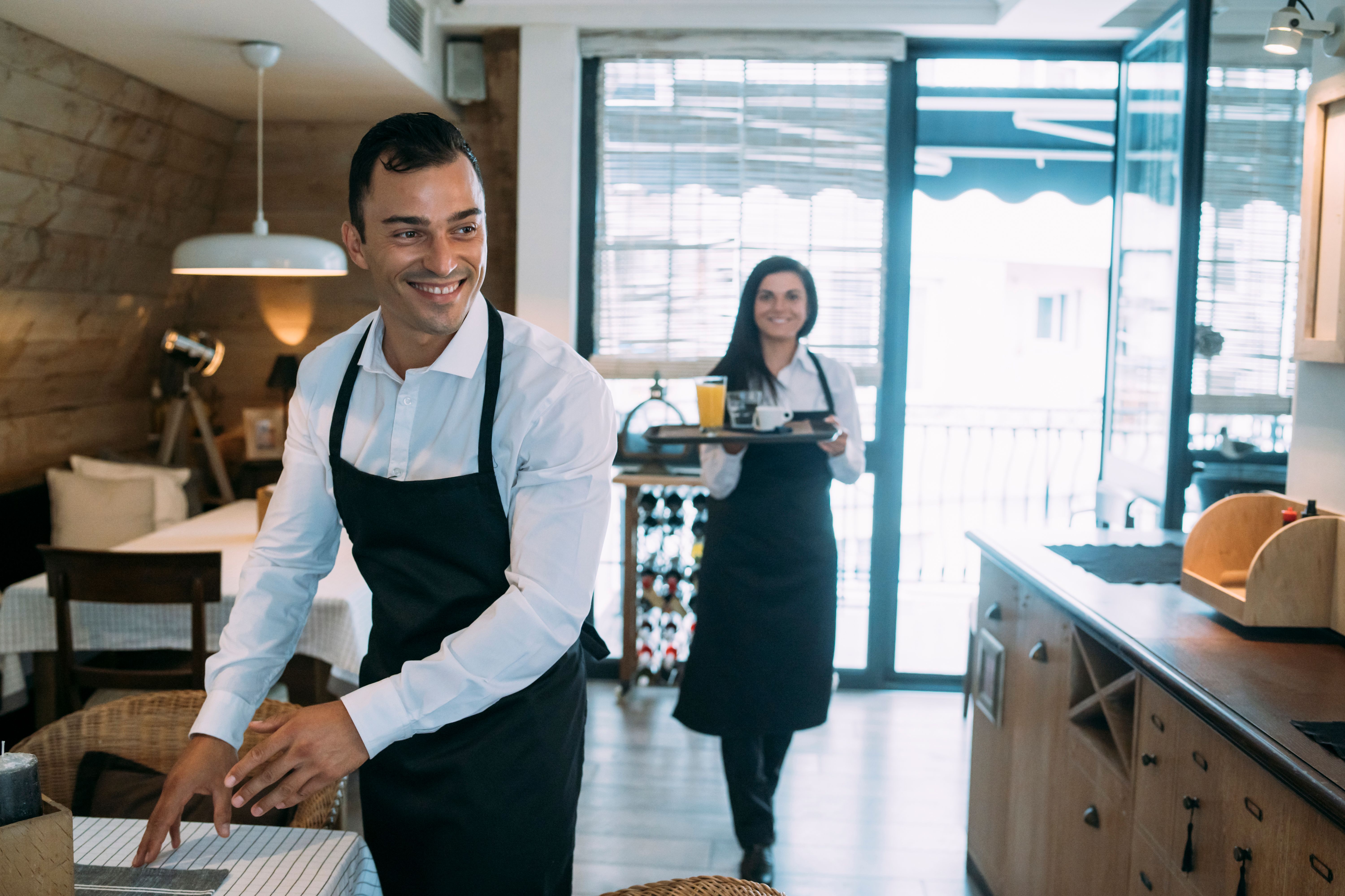 Cheerful young waiter and his female colleague during their work in the restaurant