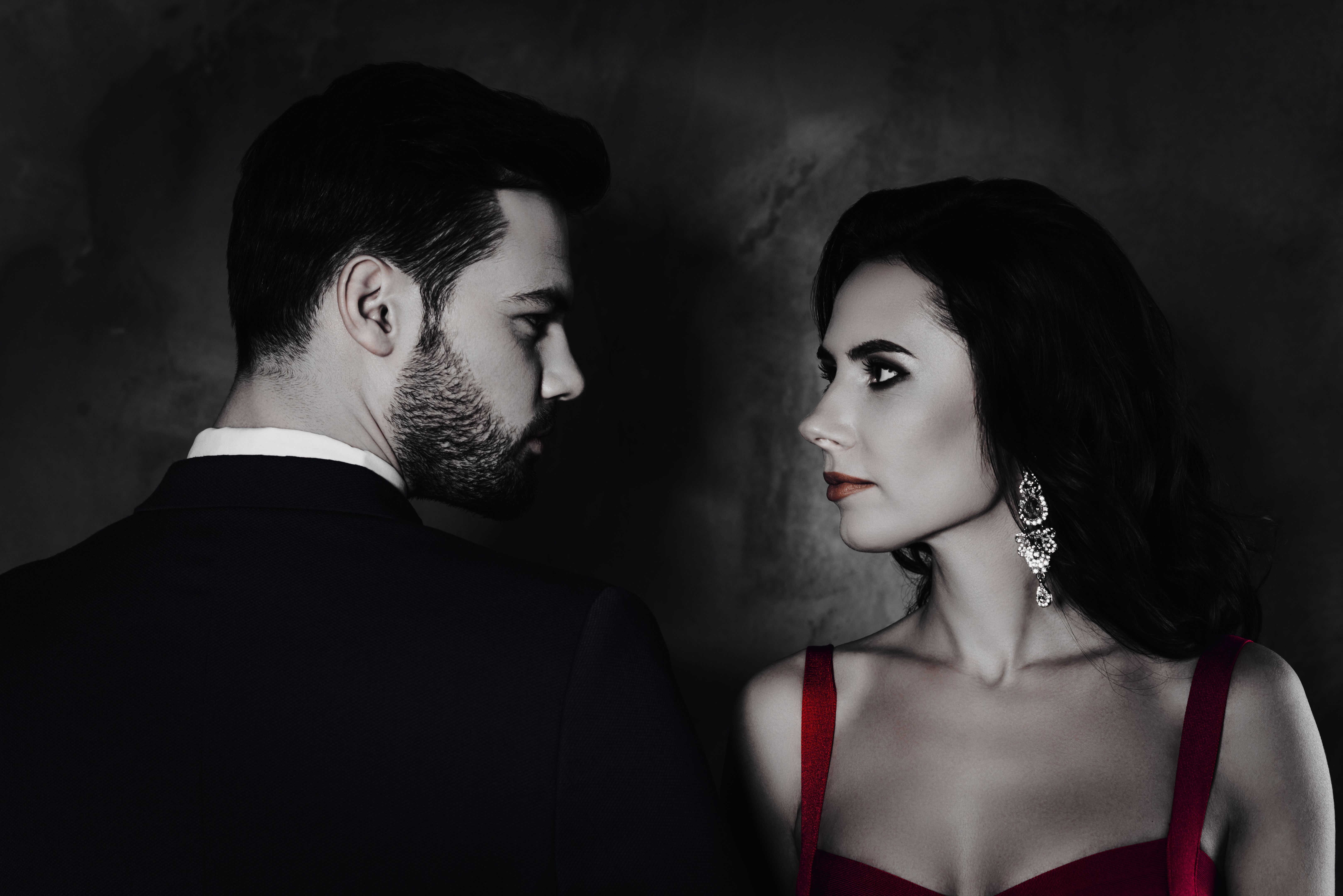 Rear view profile of brunet mr with stubble and pretty charming mrs with jewelry earring curls decollete, naughty spouses looking at each other isolated on grey background