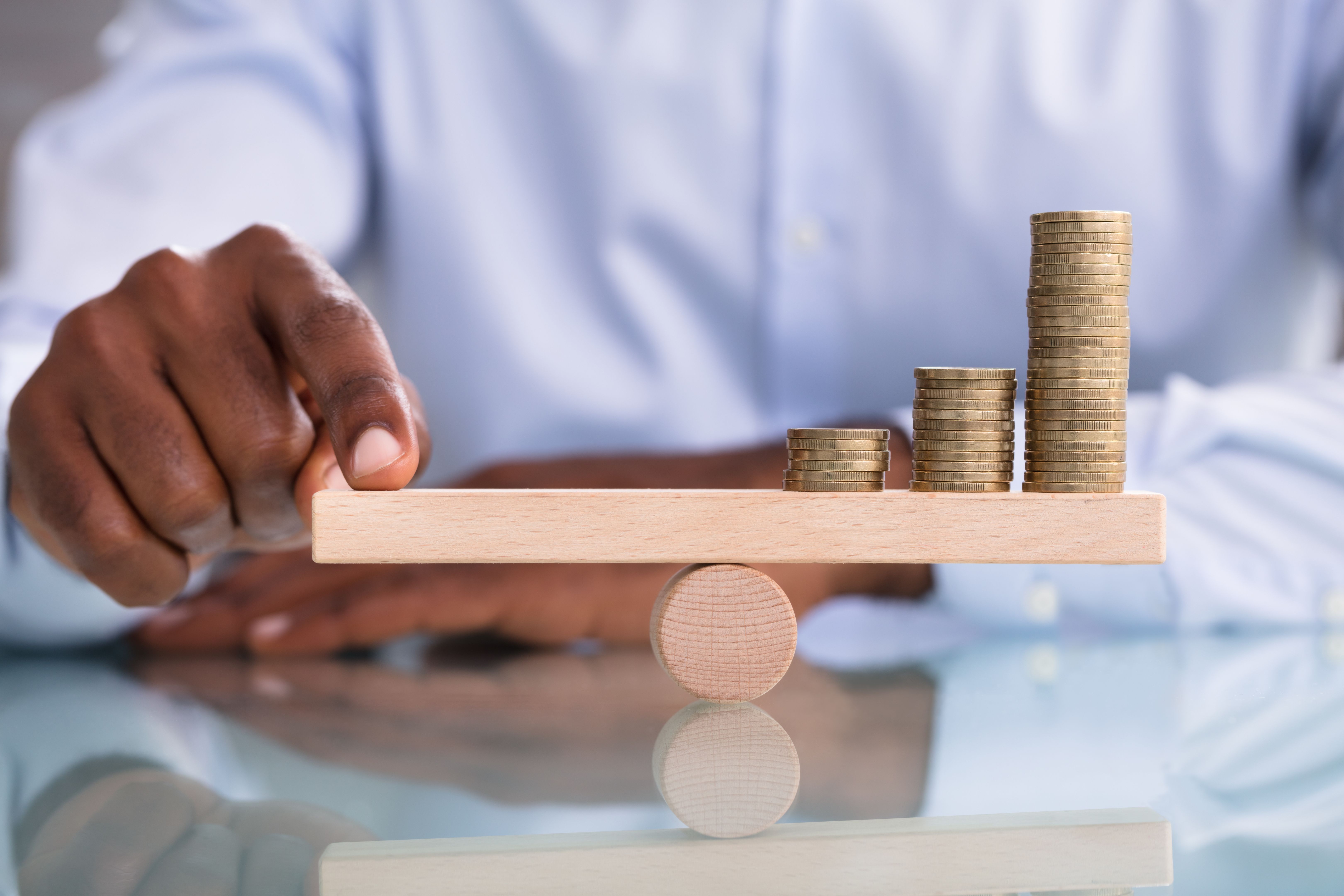Businessman Balancing The Coin Stack On Wooden Seesaw Businessman Balancing The Coin Stack On Wooden Seesaw