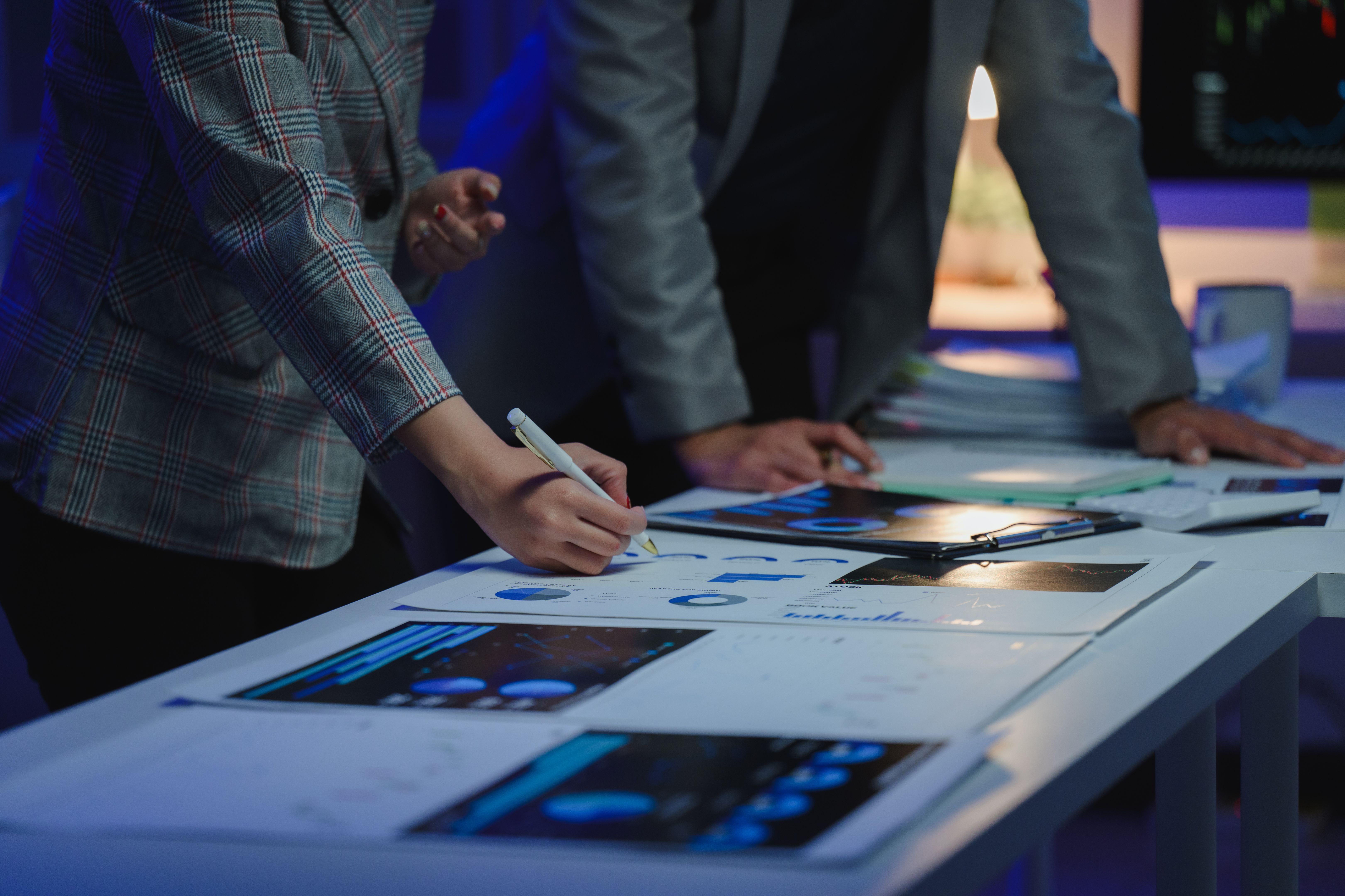 Two professionals in an office setting analyze financial documents and digital charts on a table, focusing on data-driven decision-making and teamwork