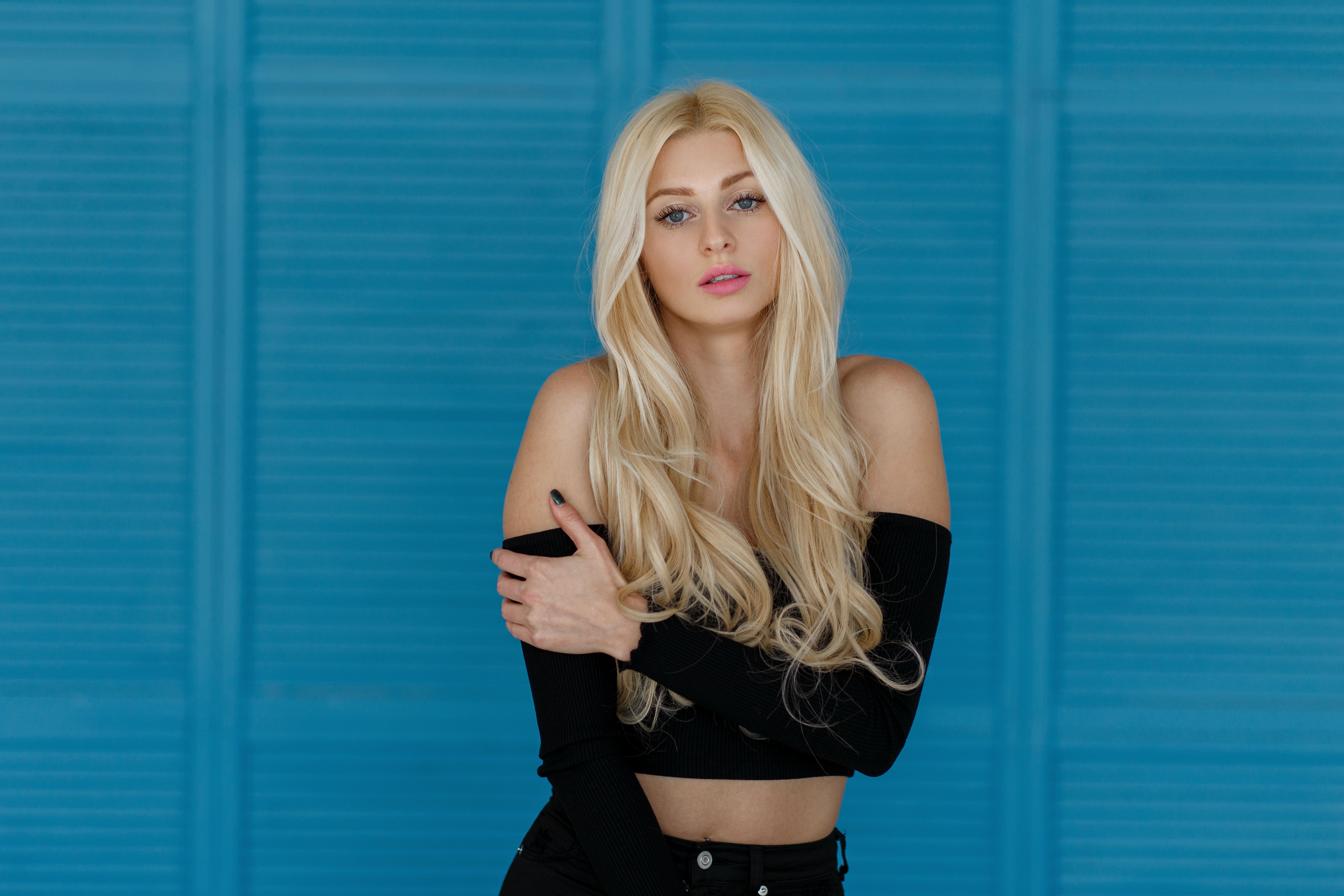 Pretty young stylish model woman with freckles with pink lips and long blond hair posing in the studio near a wooden blue wall