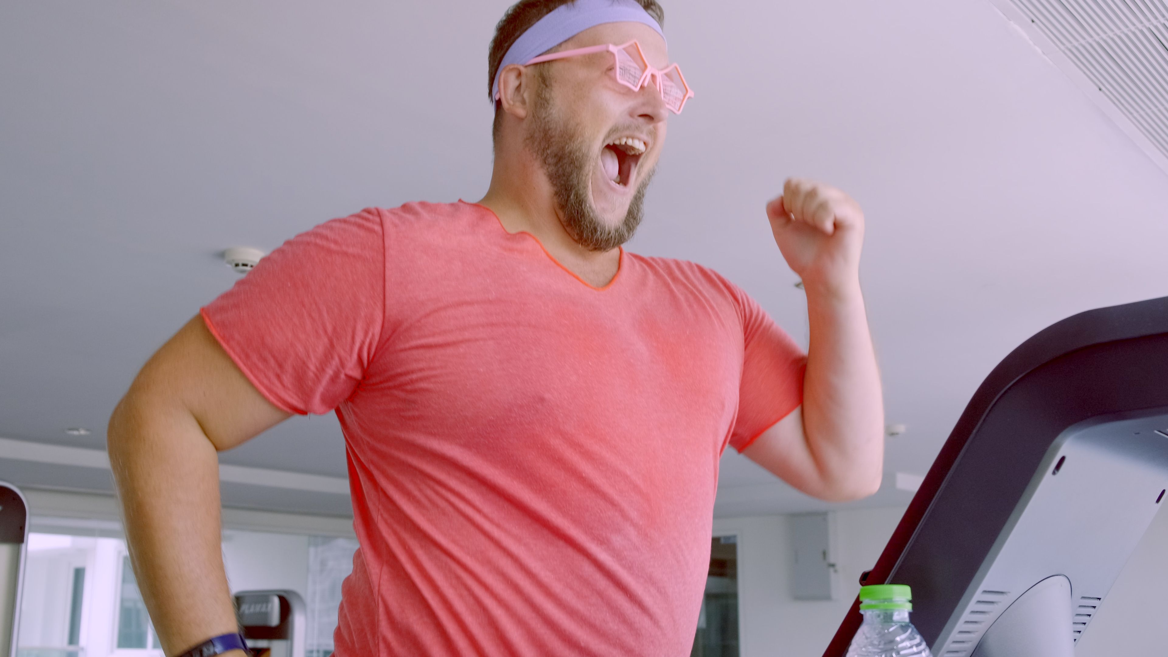 Funny fat male in pink glasses and in a pink t-shirt is engaged on a treadmill in the gym depicting a girl. 4k Funny fat male in pink glasses and in a pink t-shirt is engaged on a treadmill in the gym depicting a girl. 4k