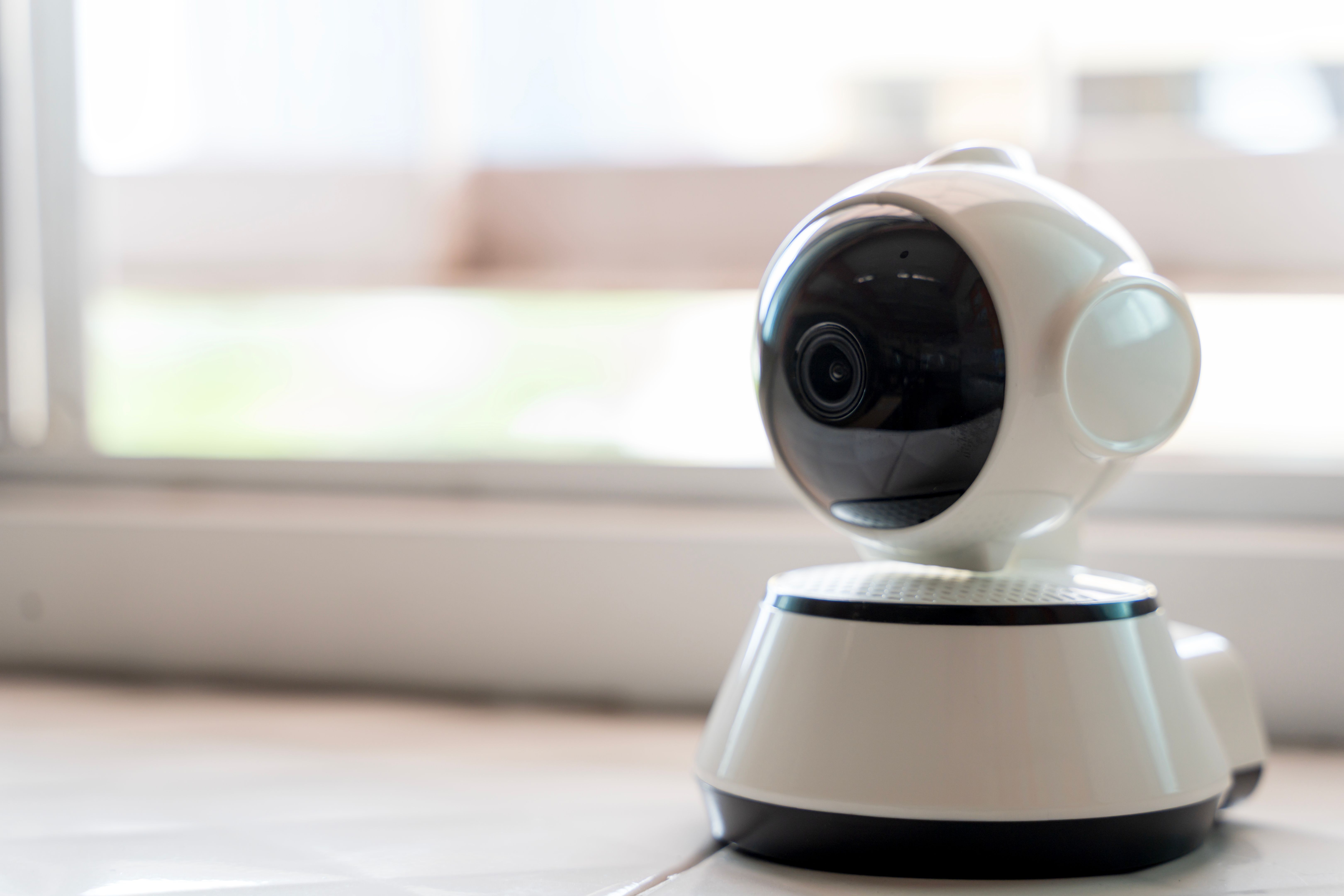 Smart indoor surveillance camera on tile floor near window for home security and remote monitoring technology
