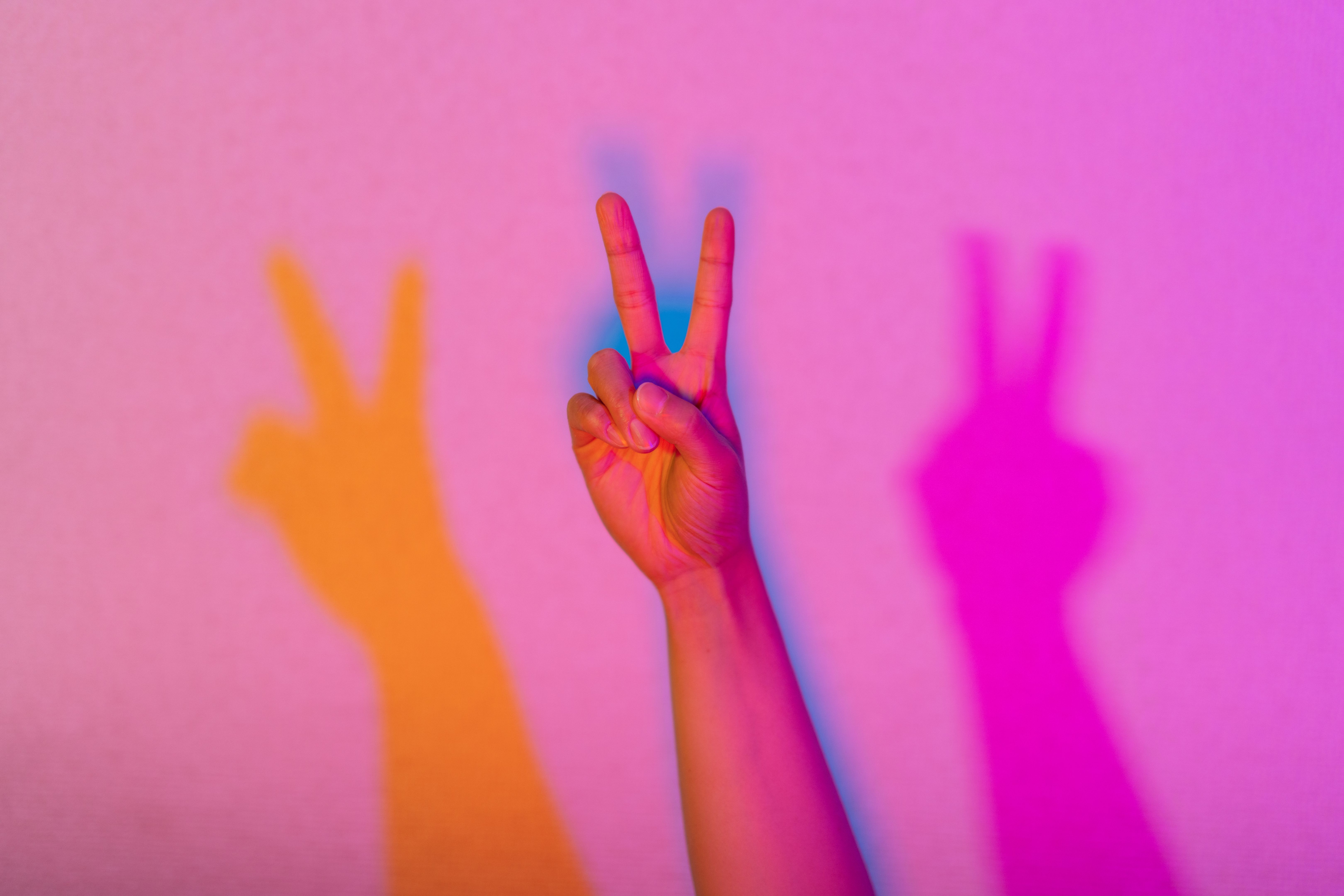 Close-up photo of hand lit by neon lights doing peace sign