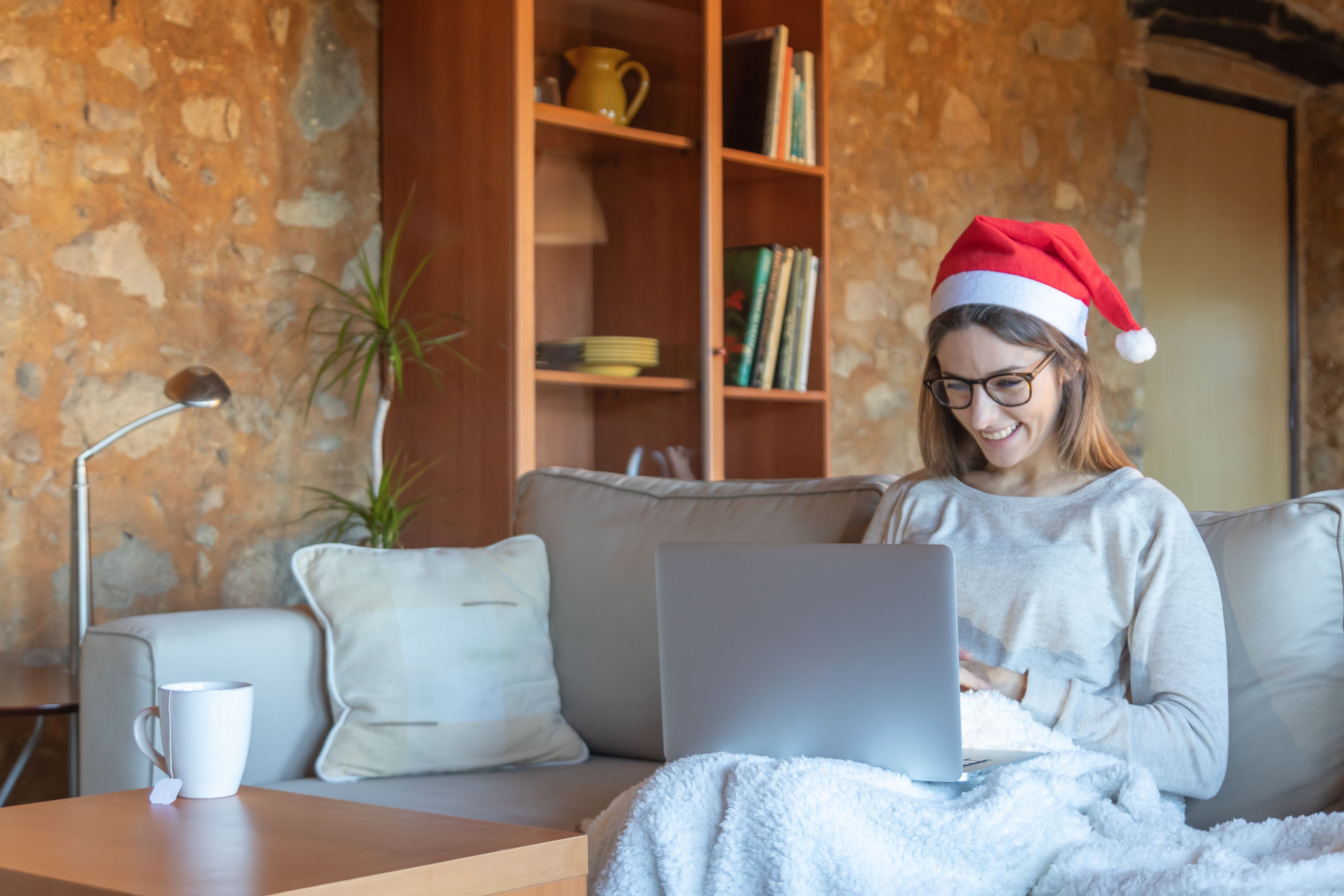 Happy young woman chatting with glasses and Santa hat sitting on the sofa at home Happy young woman chatting with glasses and Santa hat sitting on the sofa at home