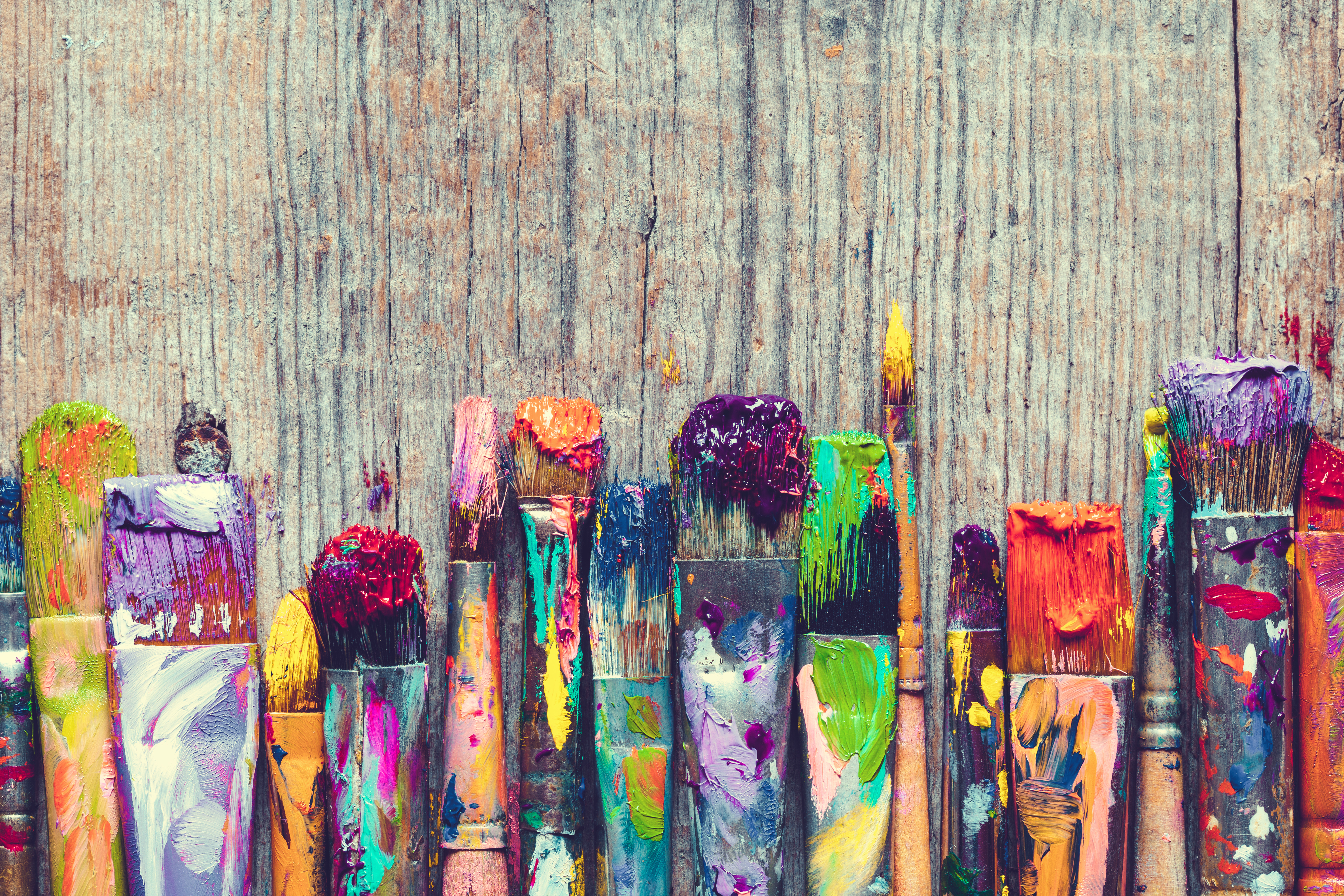 Row of artist paint brushes closeup on old wooden background.