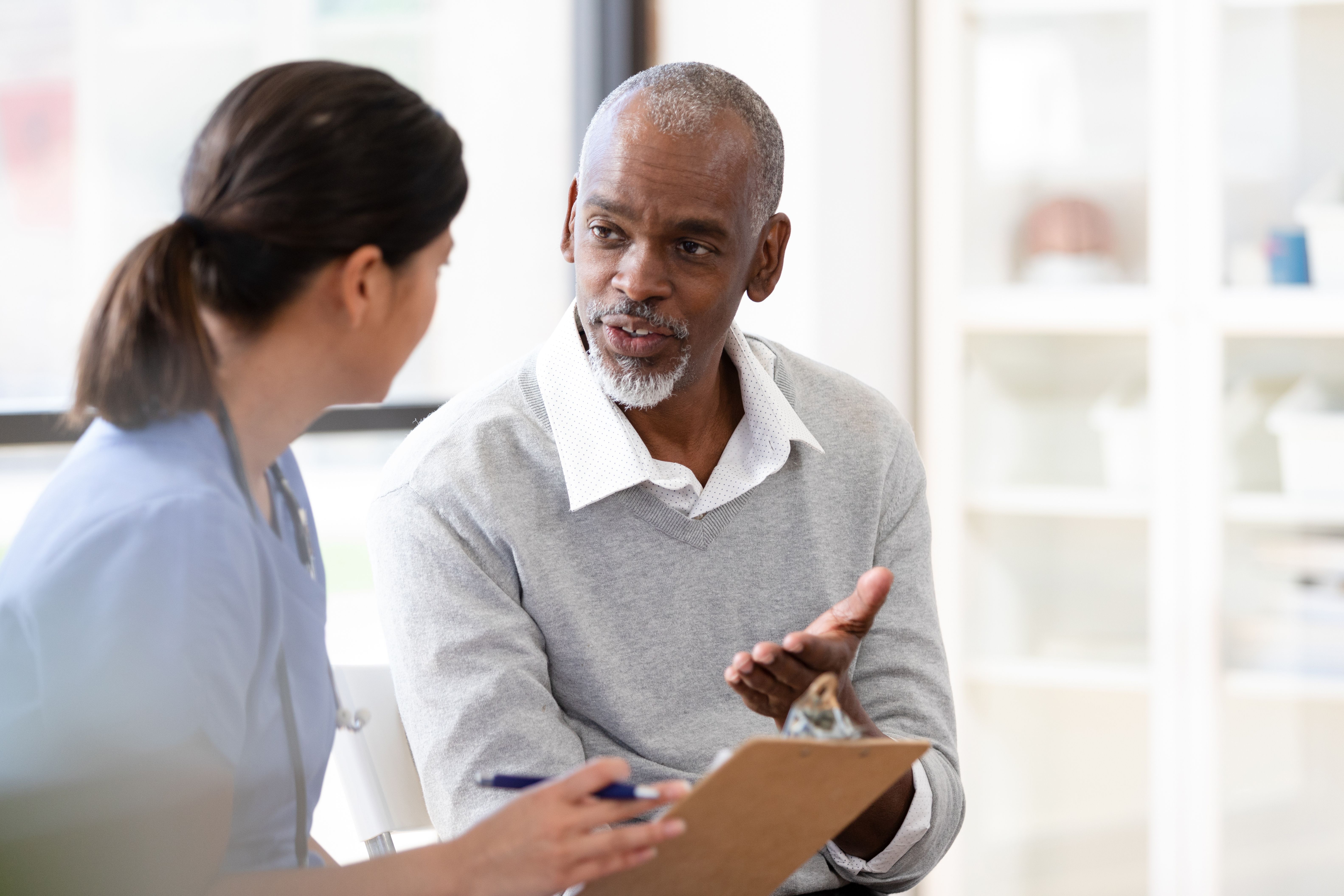 Senior man gestures while speaking to unrecognizable mid adult nurse