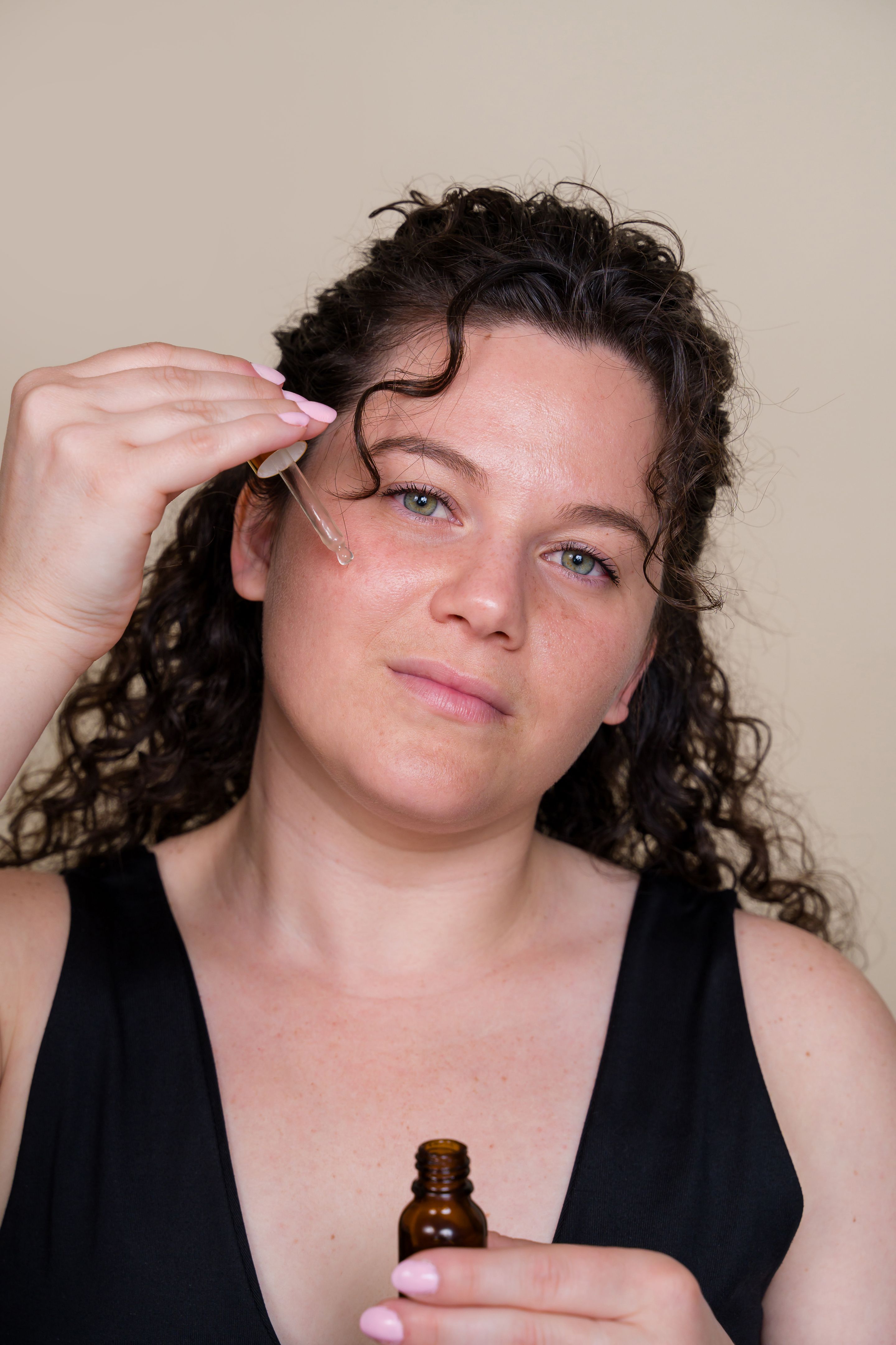 woman applying organic cosmetic serum on her face using a dropper