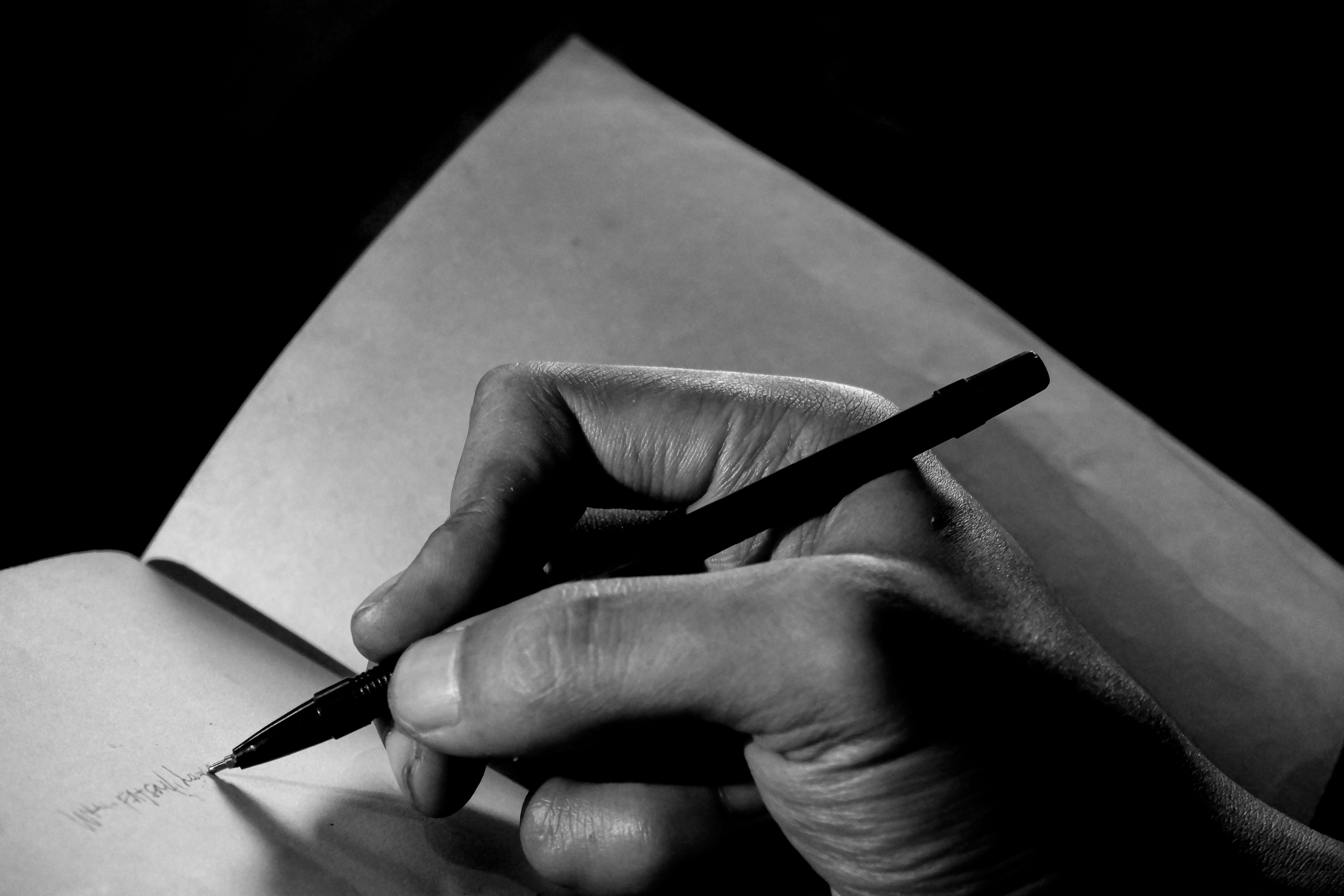 Hand Holding a Pen Writing on a Notebook Page Hand Holding a Pen Writing on a Notebook Page