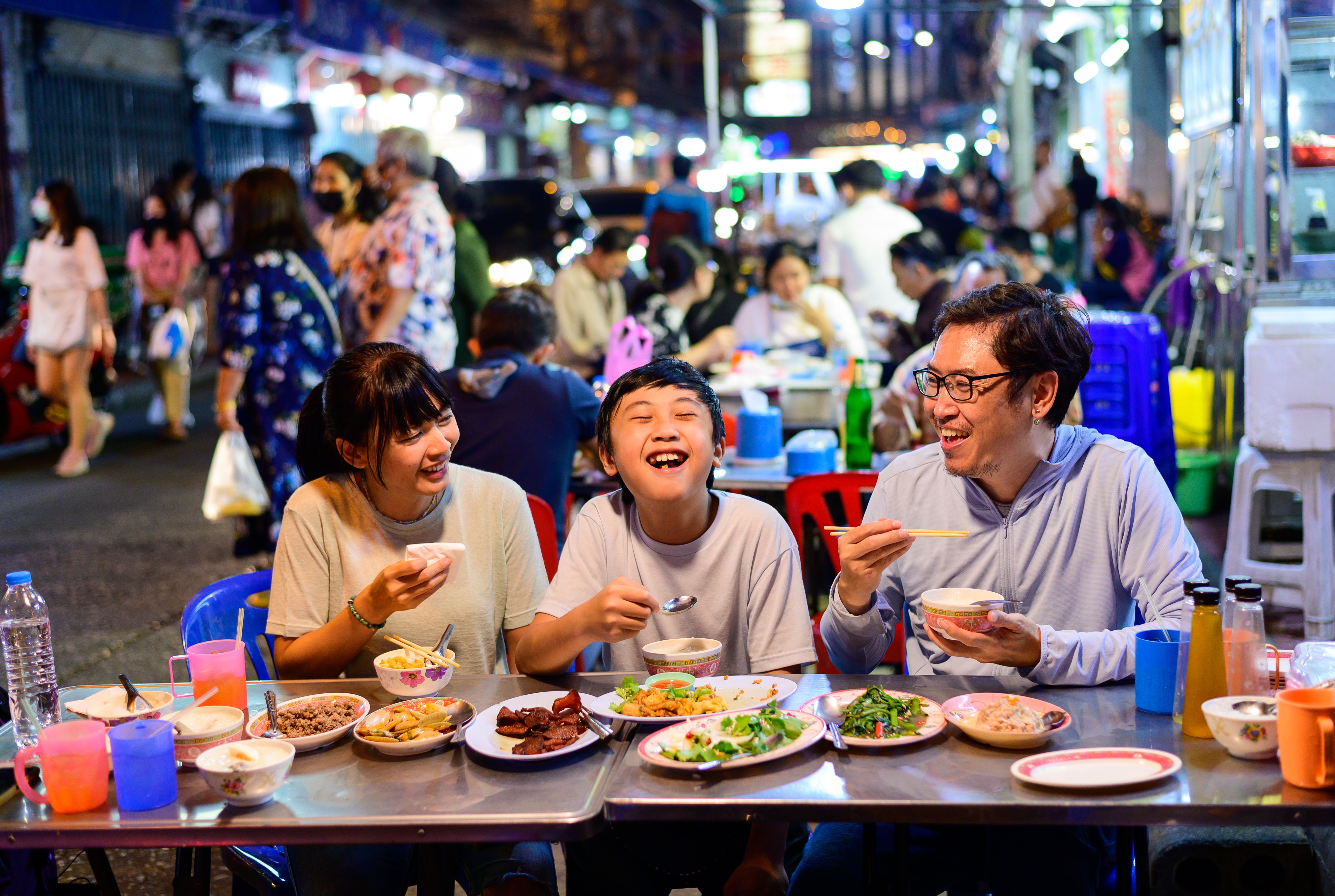 Asian family enjoy eating food on street food restaurant with crowd of people at Yaowarat road, Bangkok in Thailand