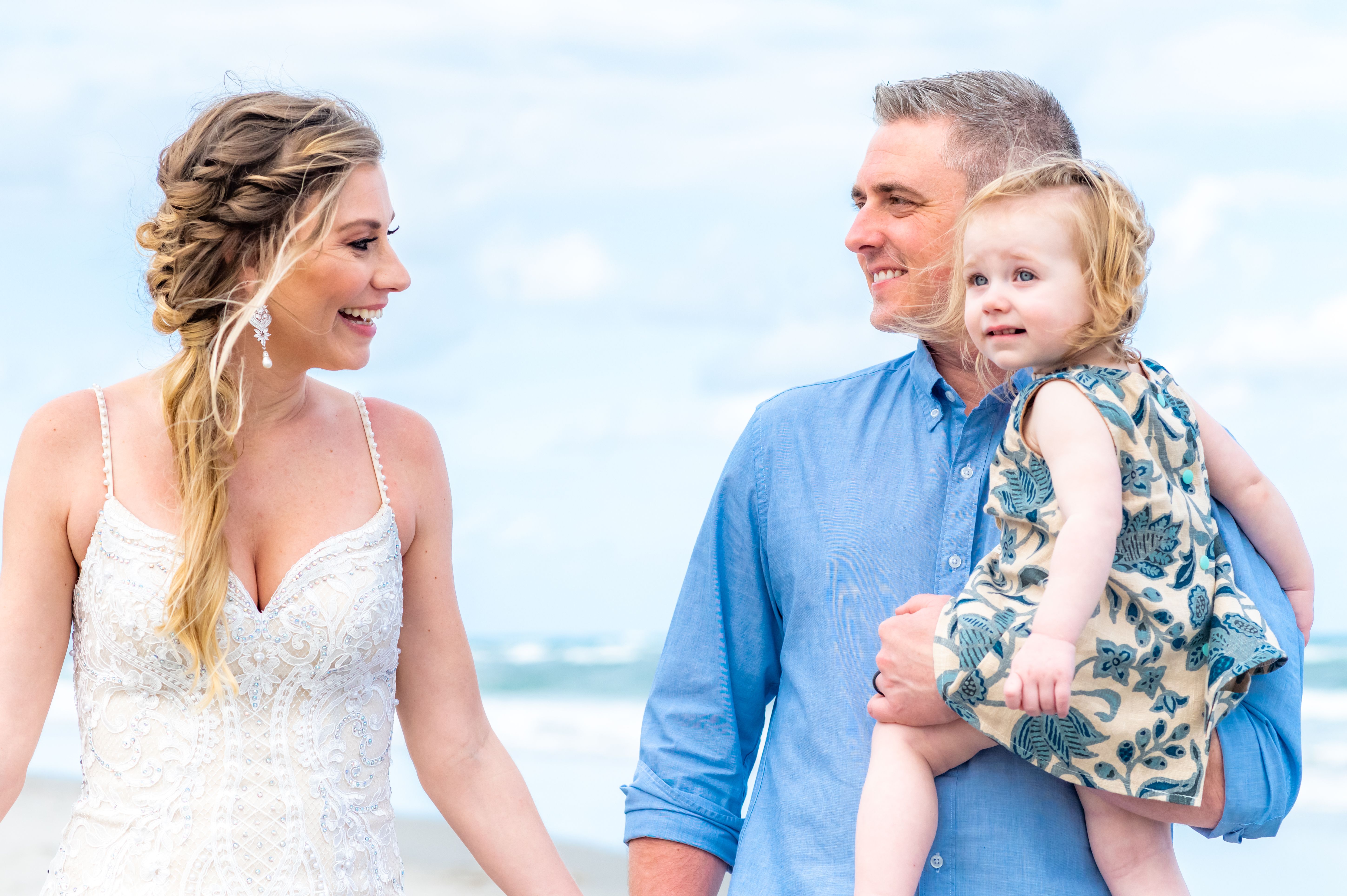 Beautiful bride holds a cute baby toddler on a beach in wedding dress. Little family destination wedding or elopement Beautiful bride holds a cute baby toddler on a beach in wedding dress. Little family destination wedding or elopement