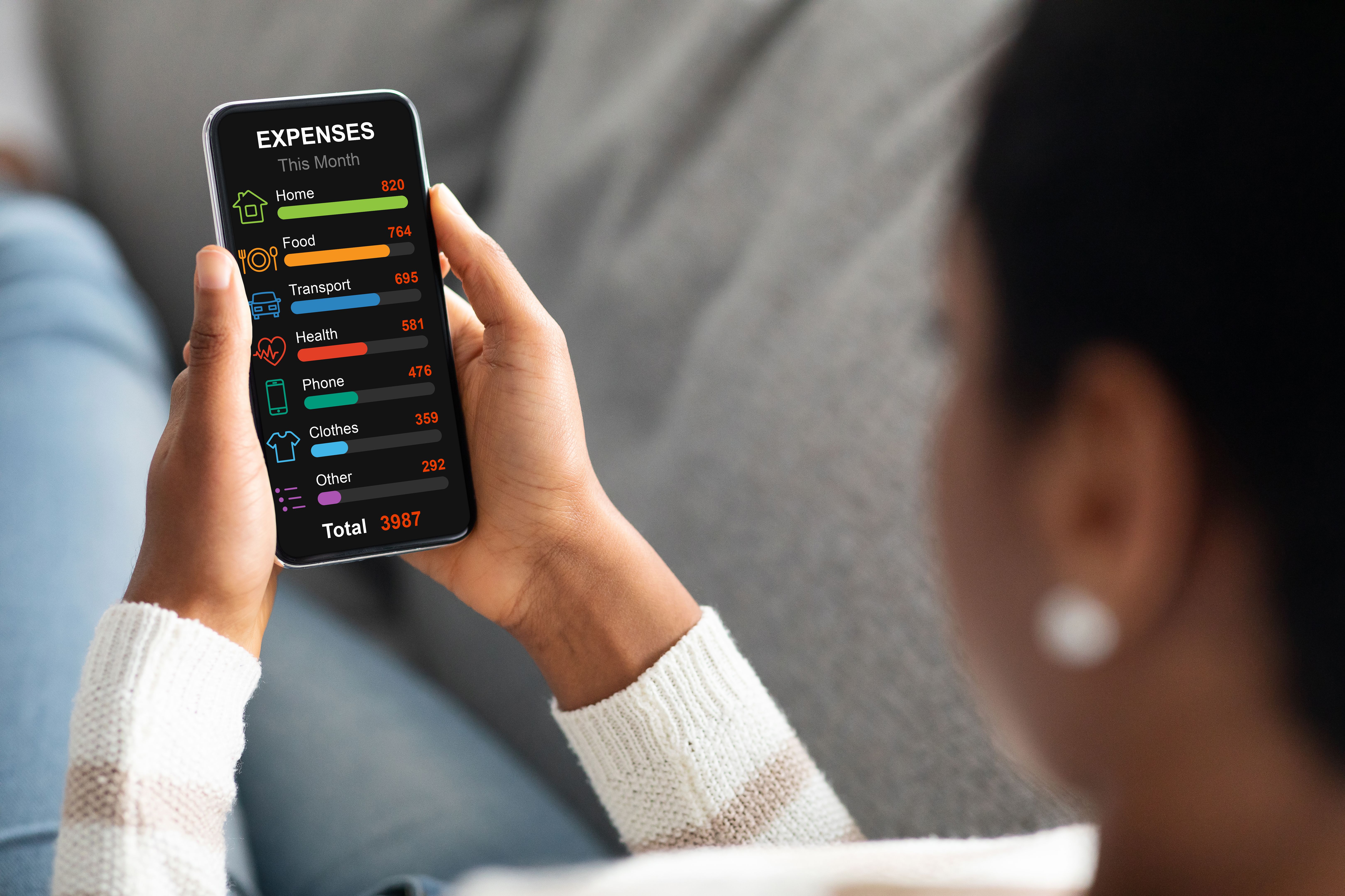 Black woman with cellphone, calculating her monthly spendings