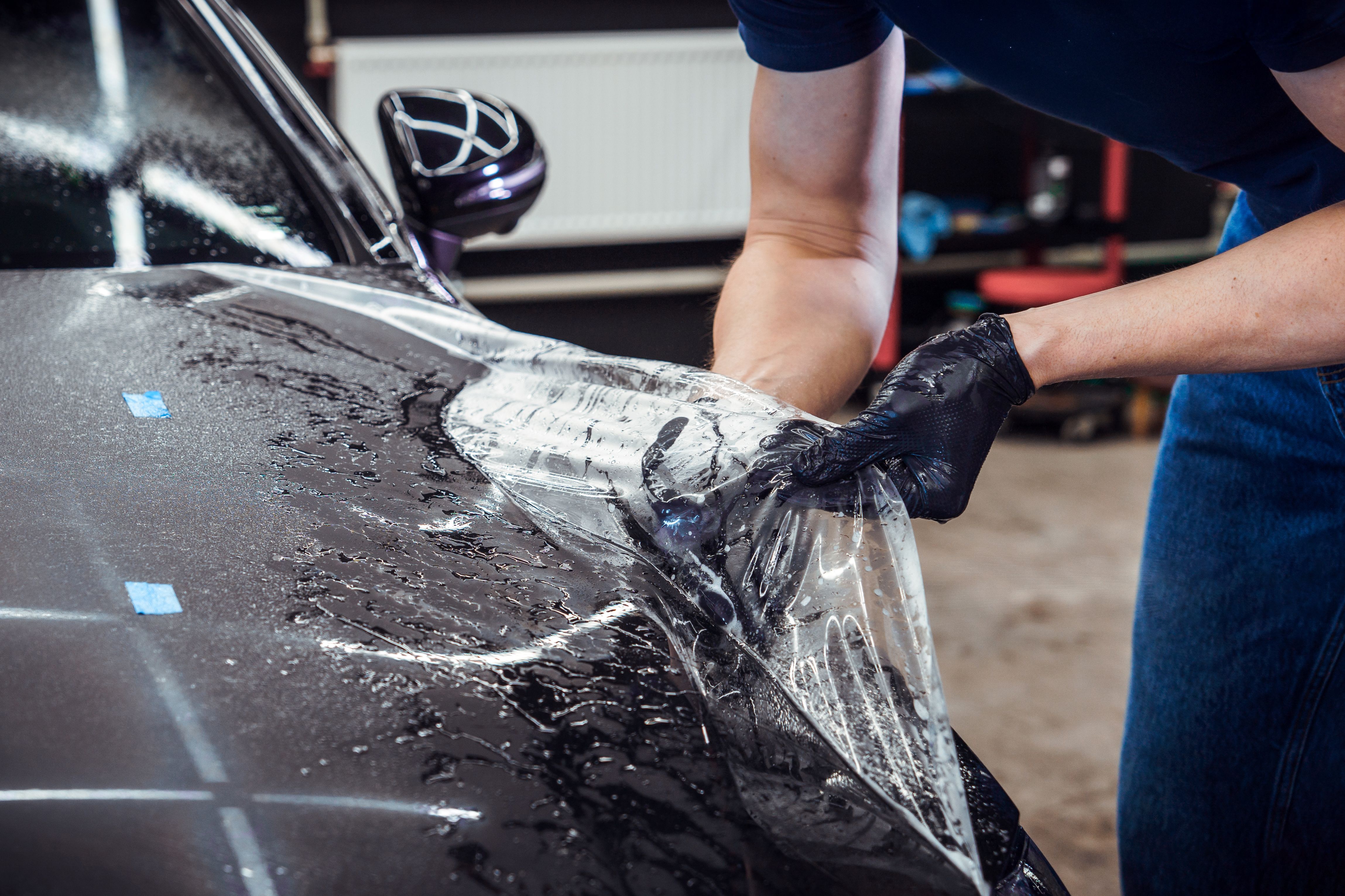 A tattooed man applies protective film to a black car