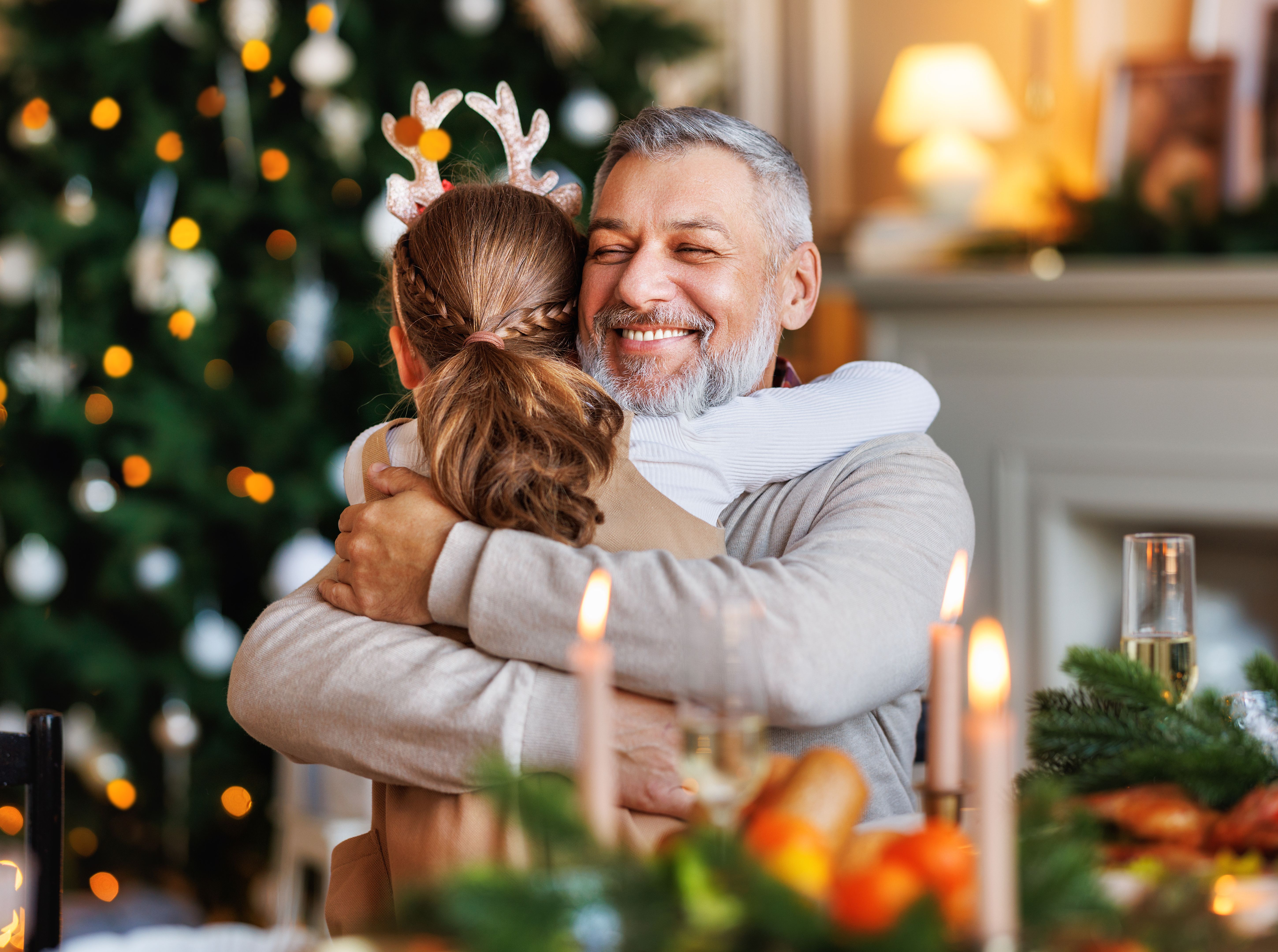 Little girl granddaughter embracing happy smiling grandfather during Christmas dinner at home Little girl granddaughter embracing happy smiling grandfather during Christmas dinner at home
