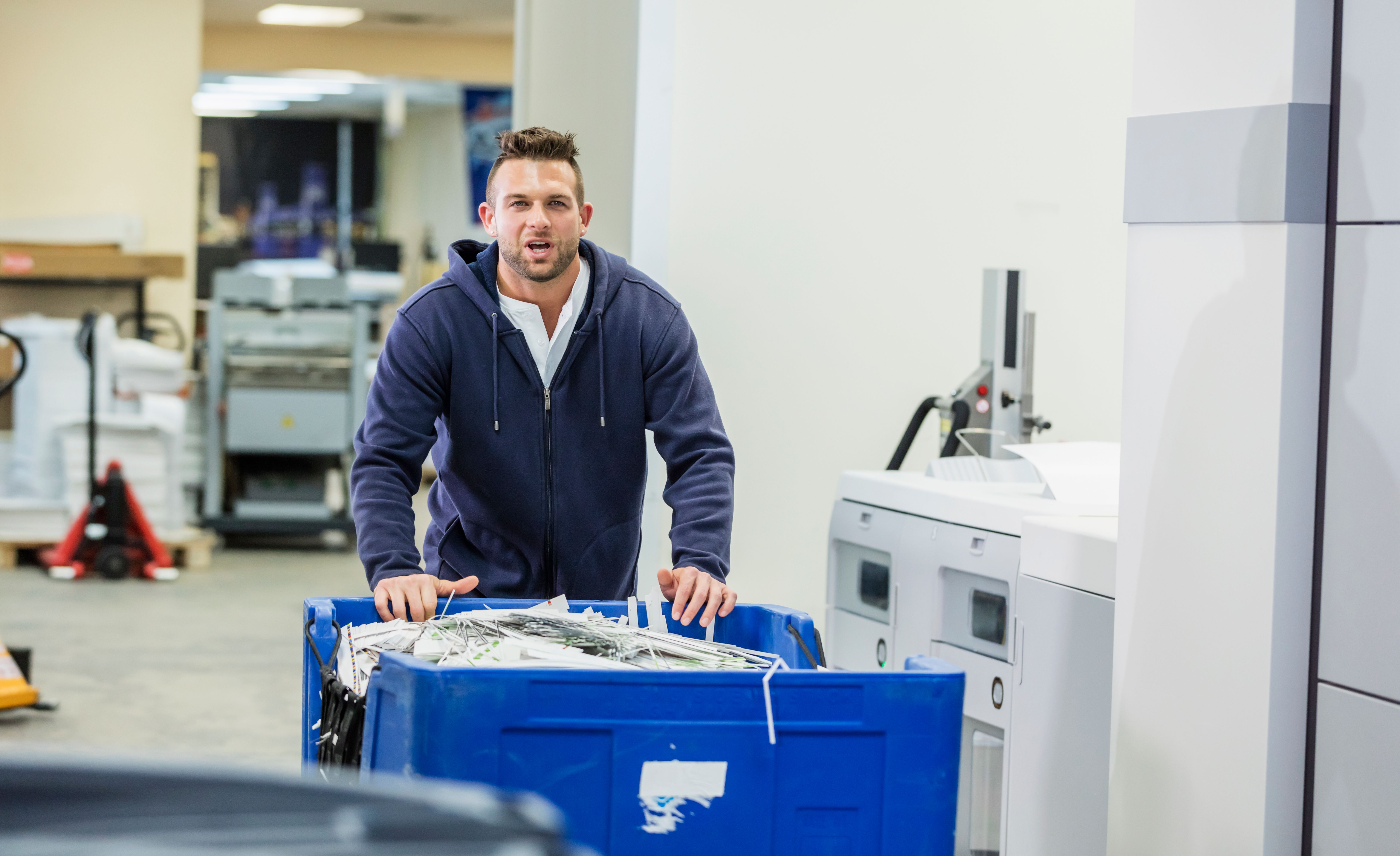 Man in printing factory with recycling bin, paper scraps