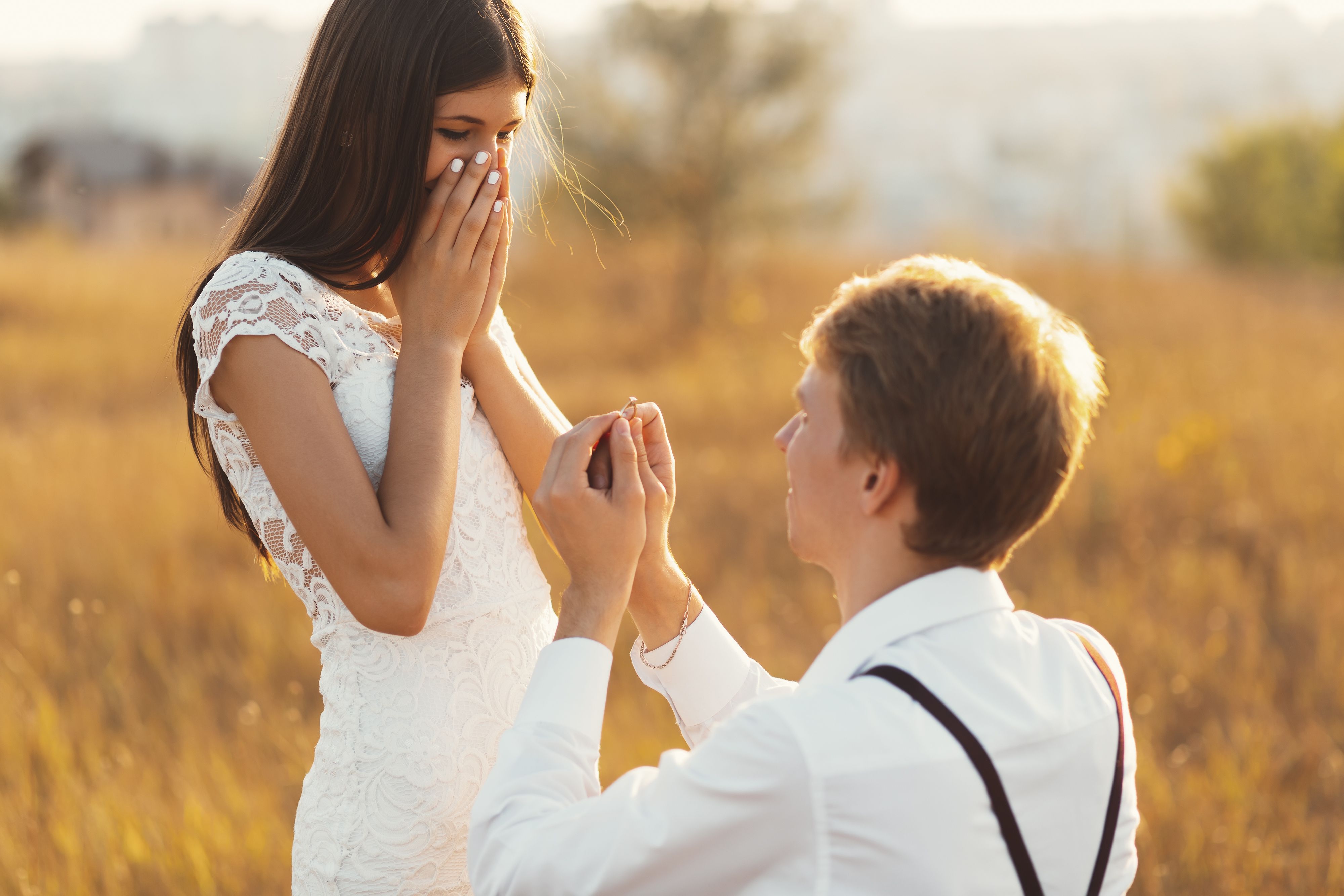 The Unique moment in their life, young man standing at his knee proposing her in a golden field outdoors. The Unique moment in their life, young man standing at his knee proposing her in a golden field outdoors.